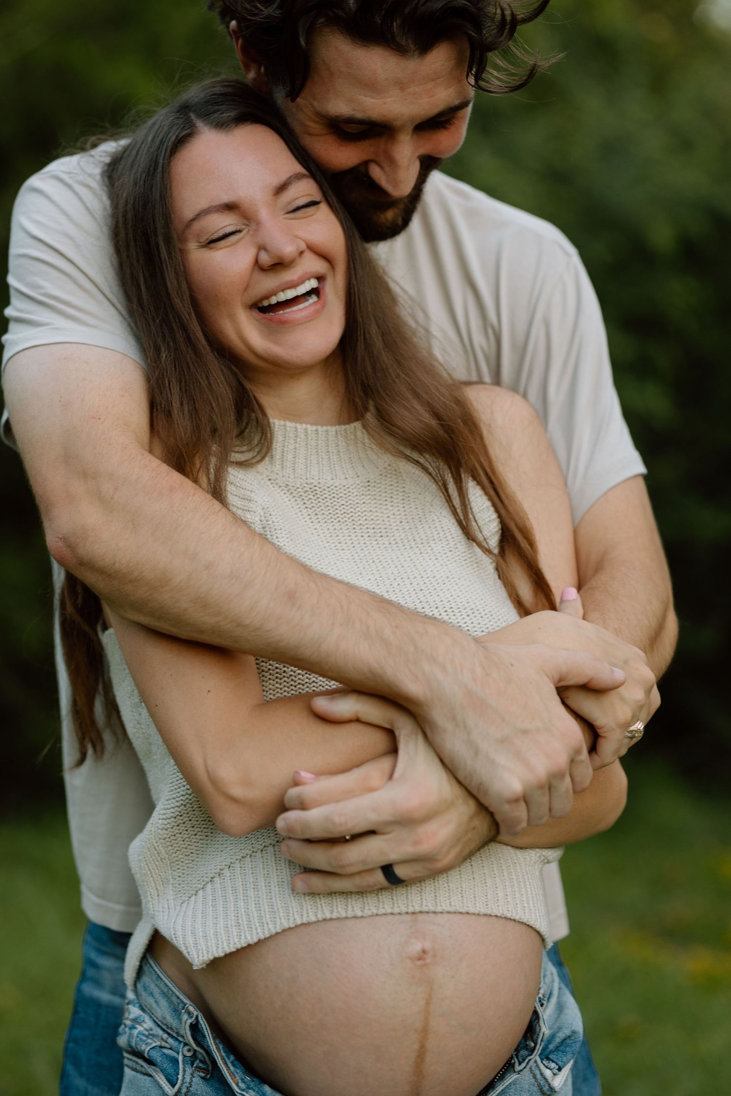 Joyful maternity moment captured of couple embracing outdoors.