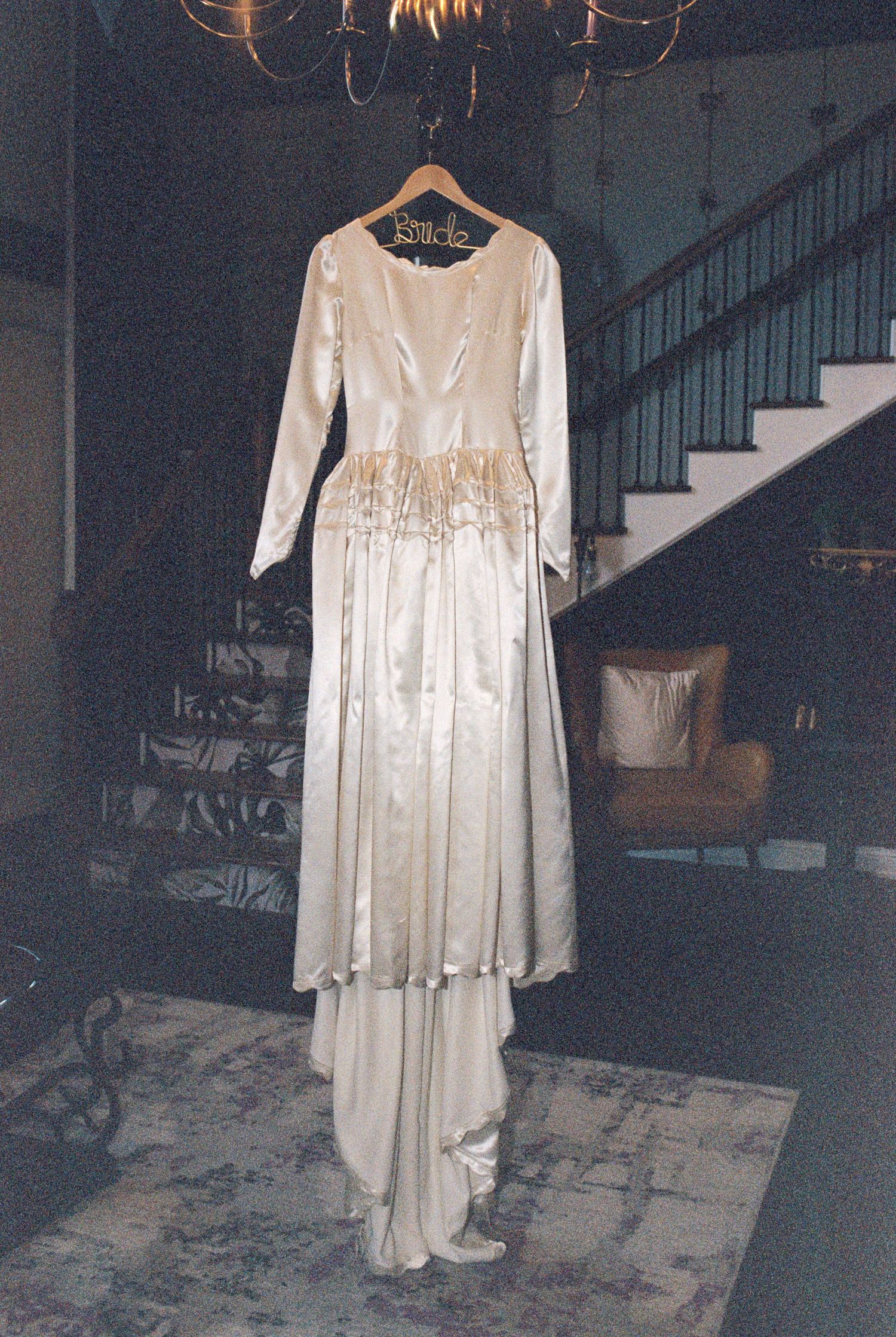 Elegant white wedding dress with long sleeves hanging on display in a dimly lit room.