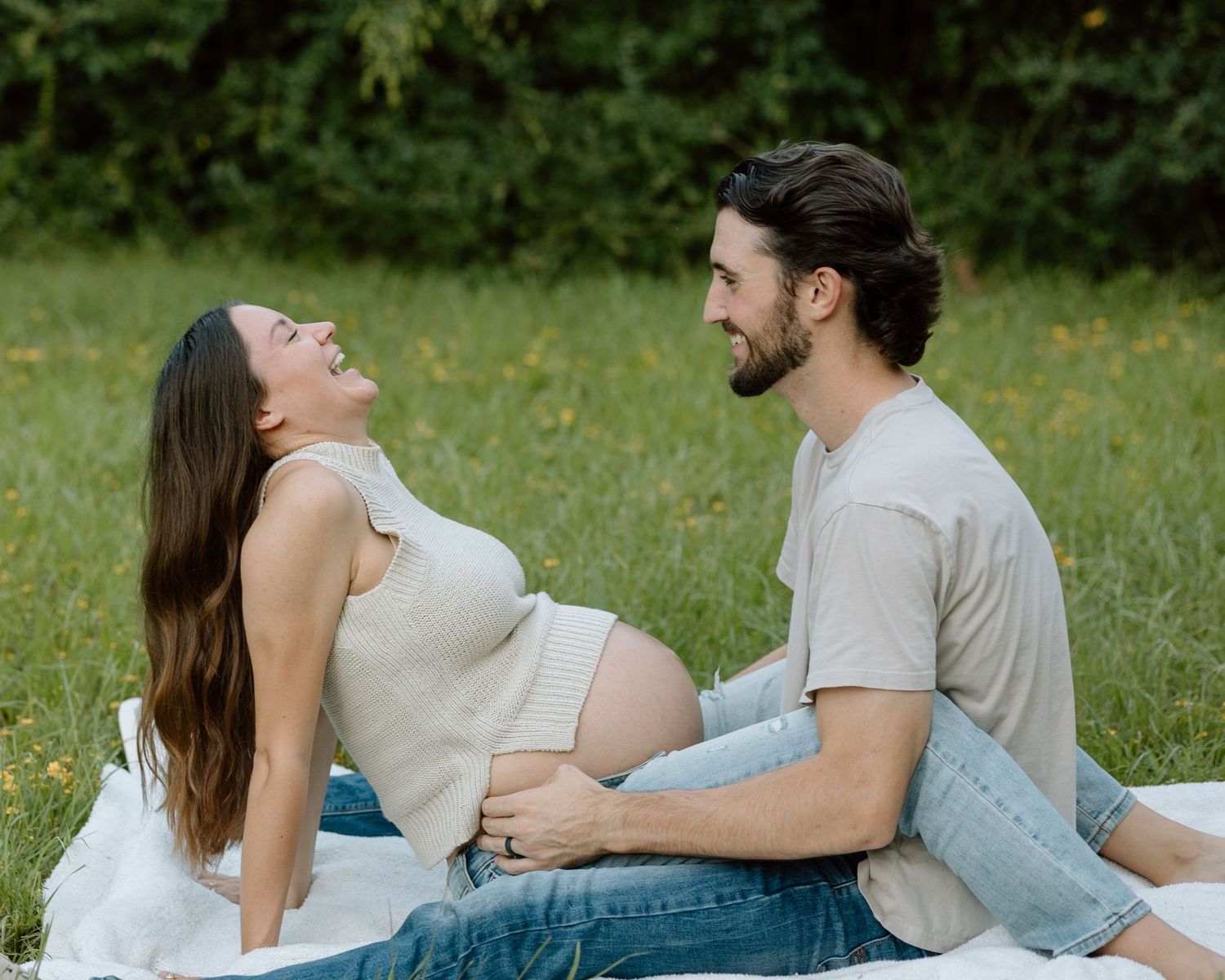A couple sitting together in a grassy field share an intimate moment during a maternity photoshoot.