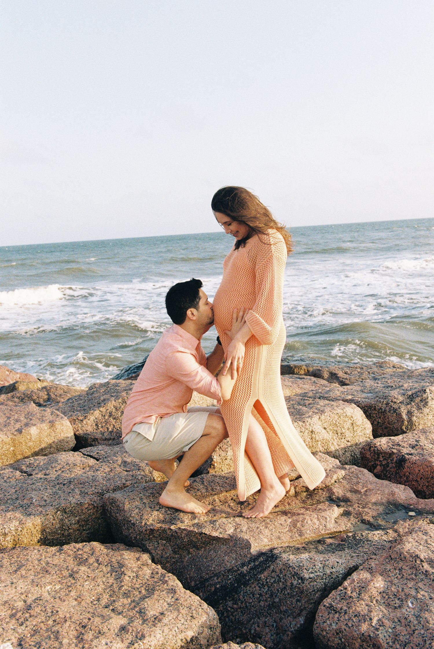 A couple shares an intimate moment on rocky beach during sunset.