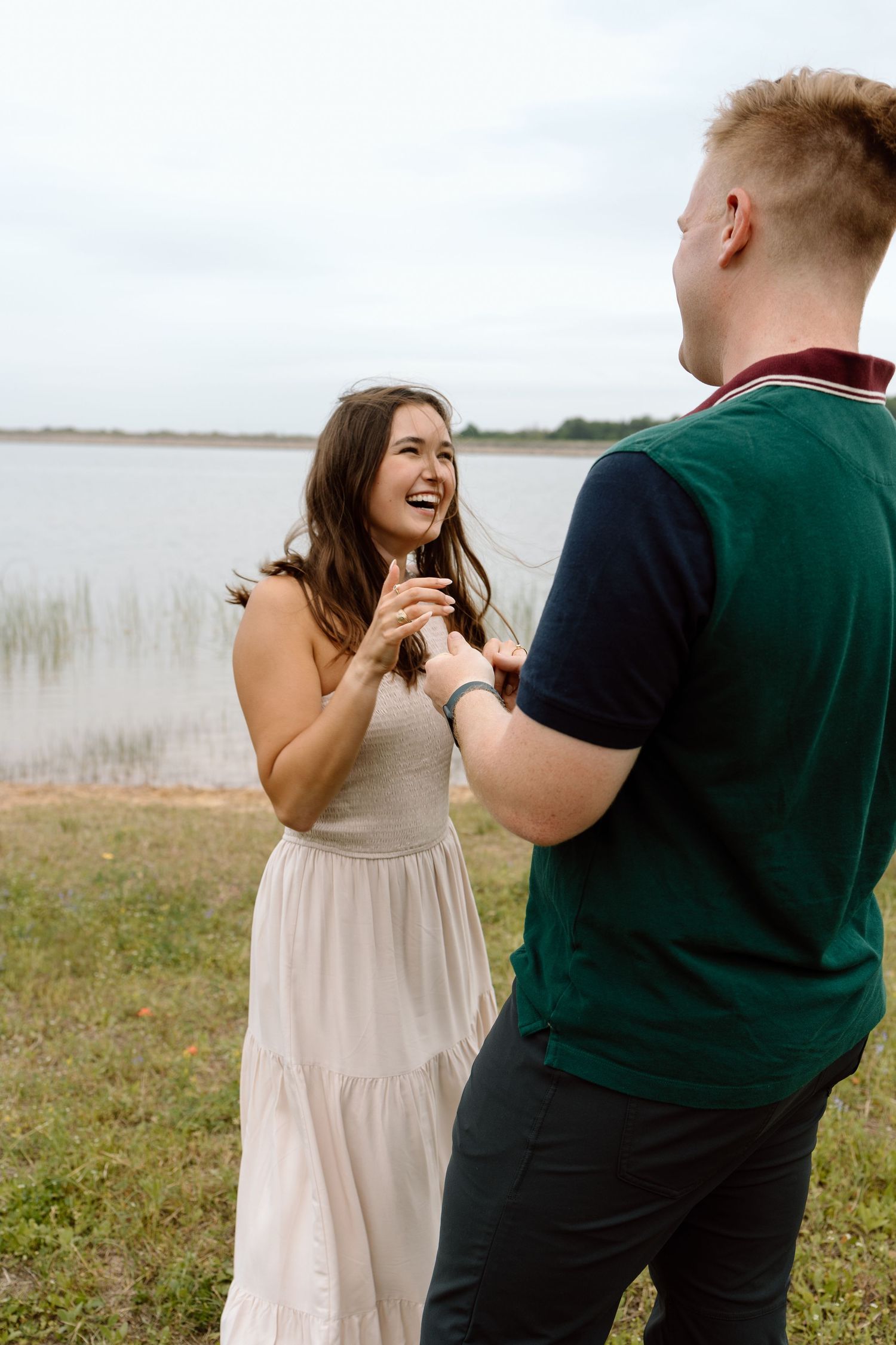 A couple laughs together during a romantic moment by a lake.