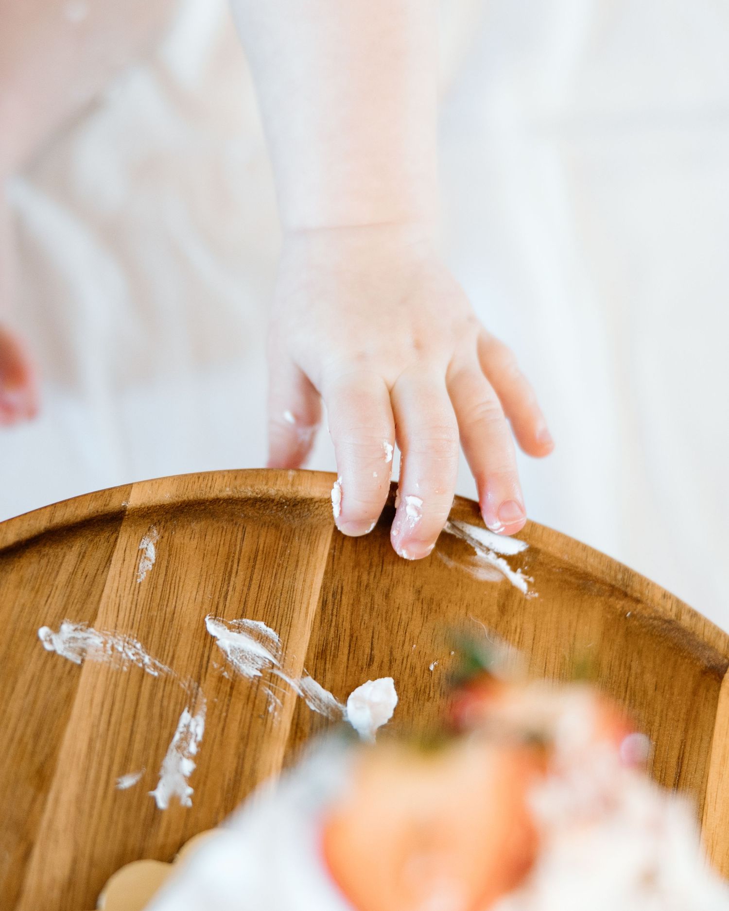 A child's hand with white frosting on a wooden plate during a cake smash photo session.