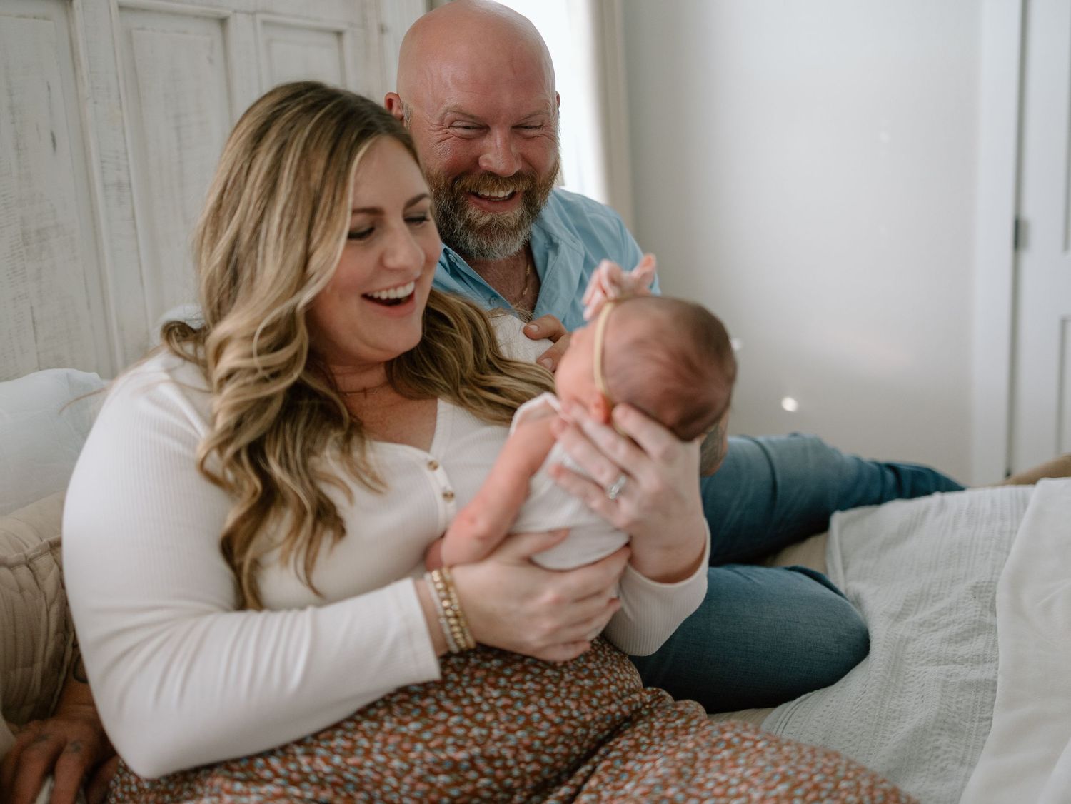 A couple relaxes at home on a cozy couch while holding and admiring their newborn baby together.