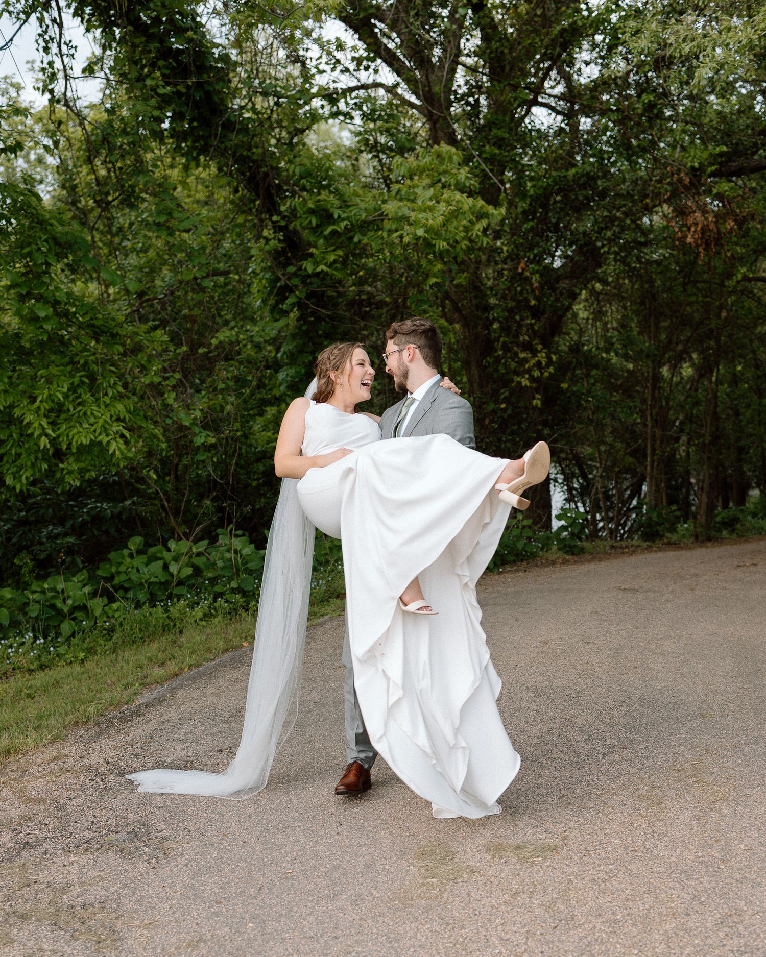 Joyful wedding photo on garden path showing romantic lift pose surrounded by greenery.