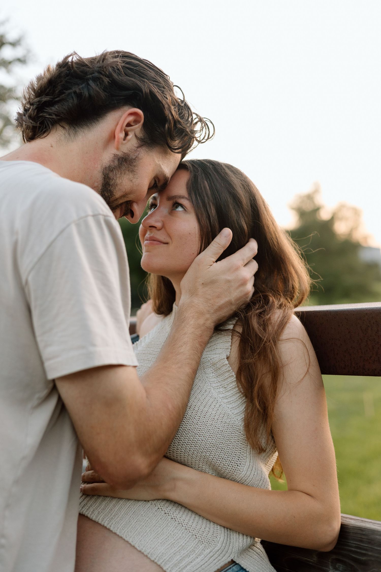 Intimate closeup of expecting couple sharing a tender moment on wooden bridge.