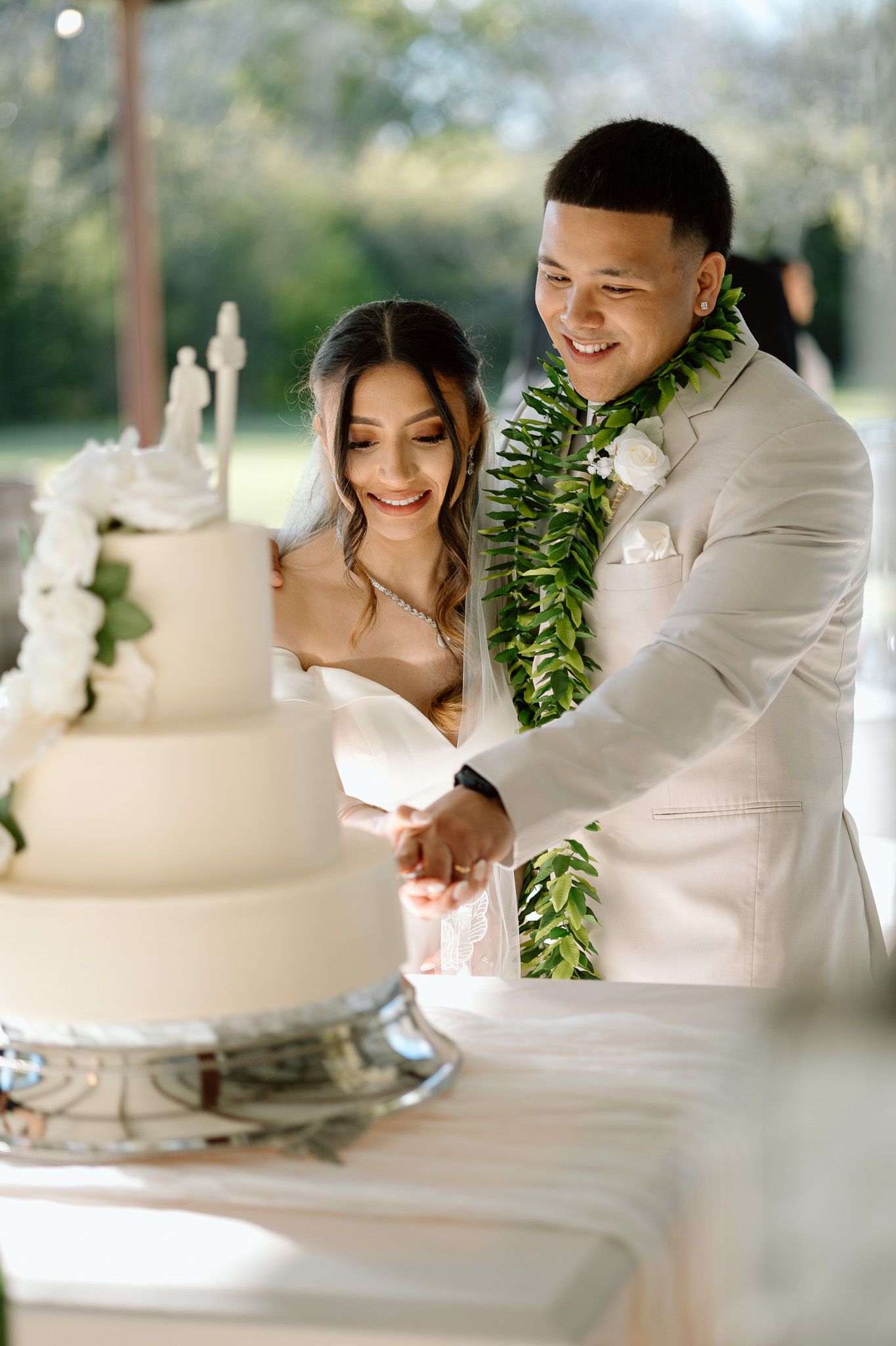 Newlyweds cut their white wedding cake together at outdoor reception.