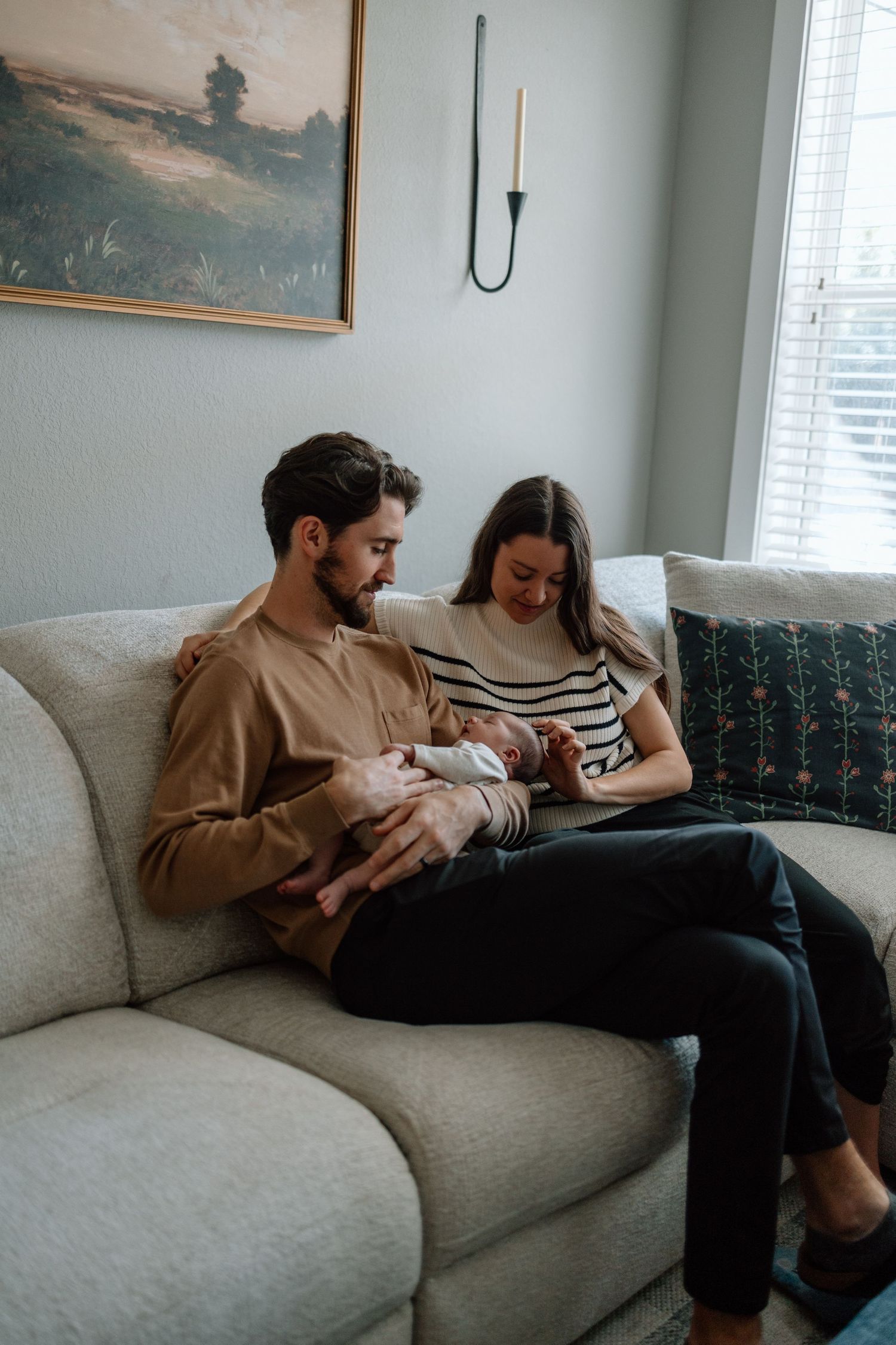 Loving parents sitting on beige couch with newborn baby in cozy living room setting.