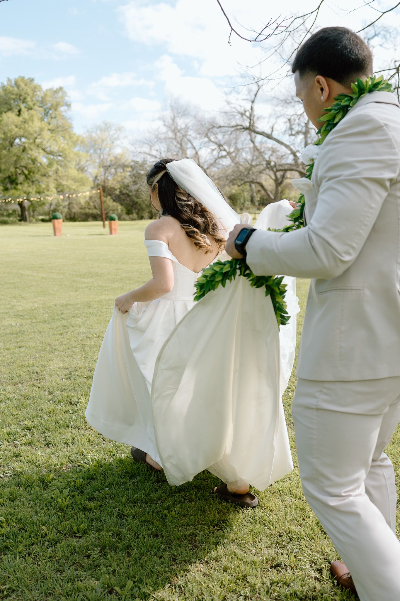 A couple in white attire dancing together on grass during their wedding celebration.