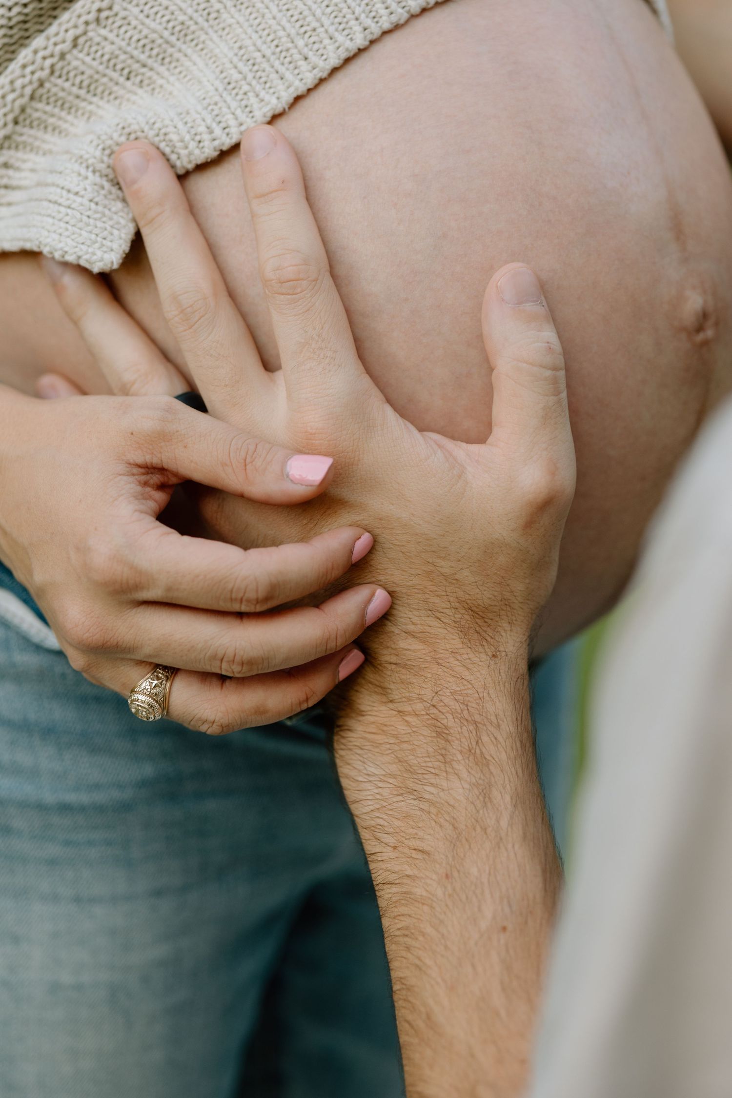 Close-up of hands resting on a pregnant belly wearing a knit sweater.