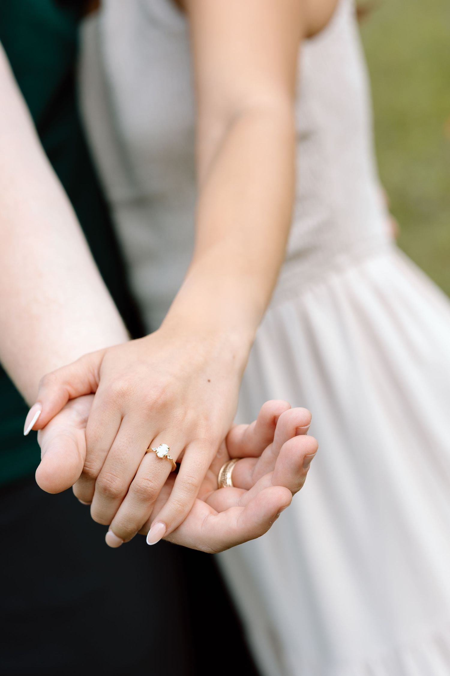 Close-up of intertwined hands showing off an engagement ring against a white dress documentary photography college station Texas.