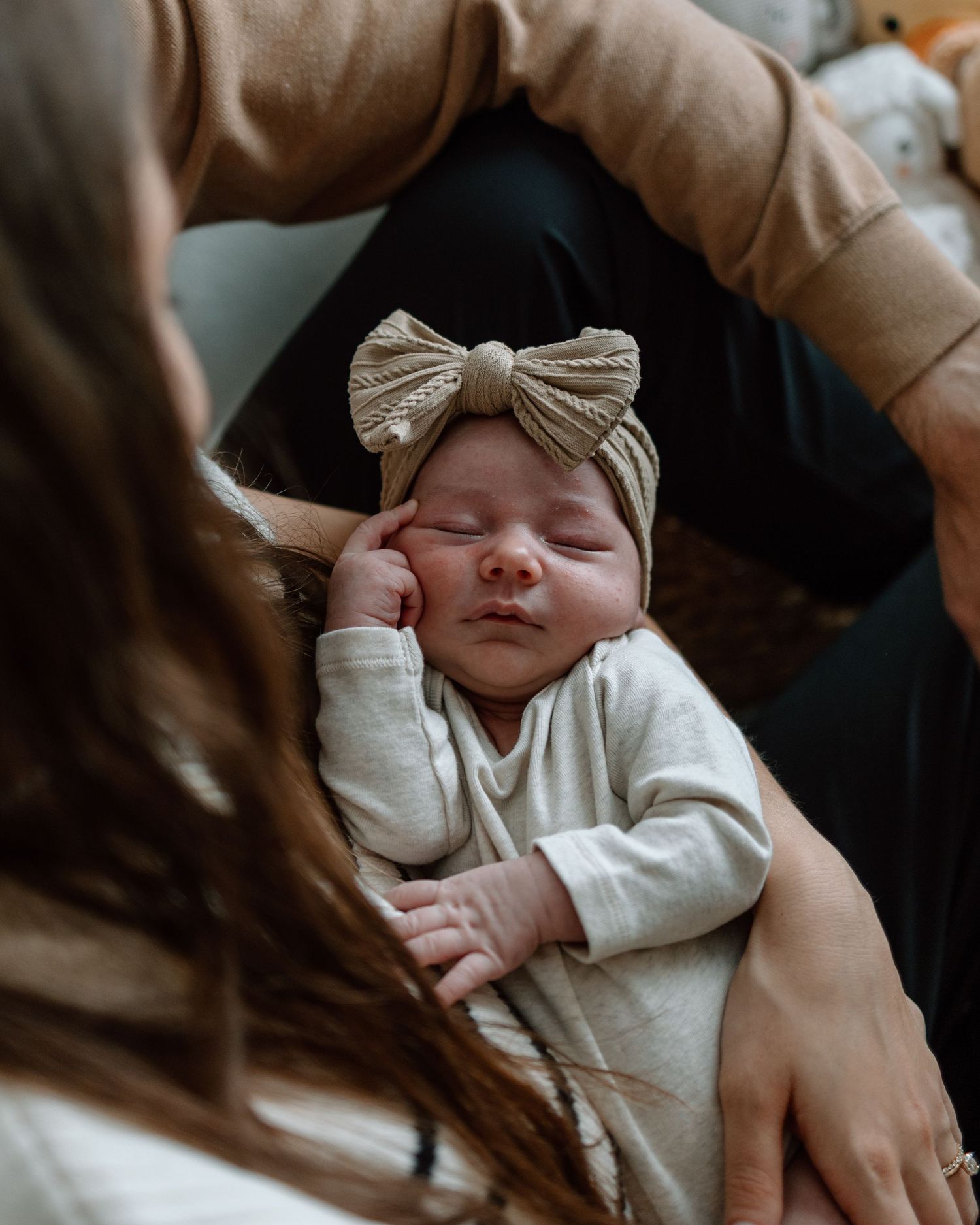 Sleeping newborn wearing white outfit and gold bow headband being held.