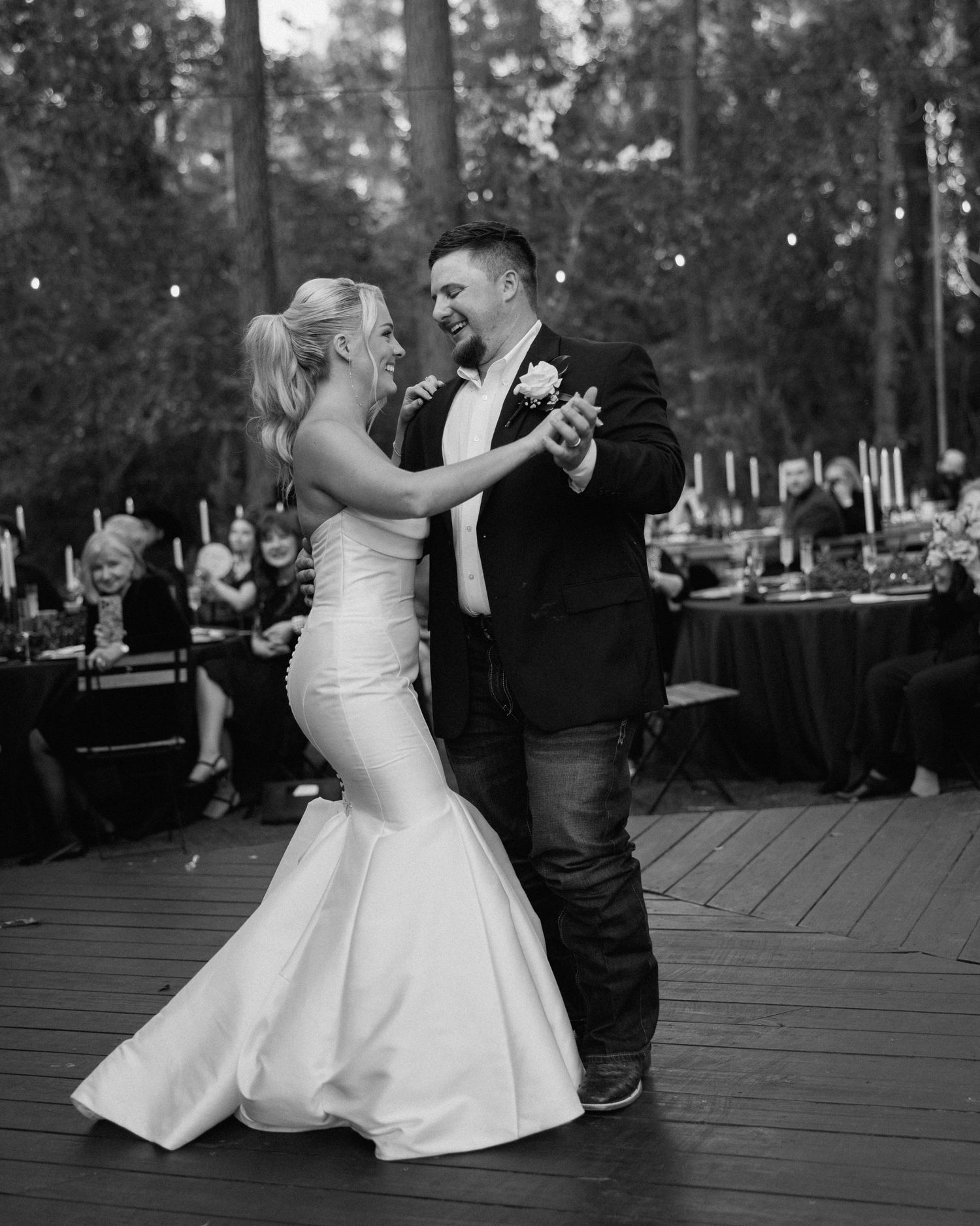Bride and groom share first dance on outdoor wooden dance floor at evening reception.