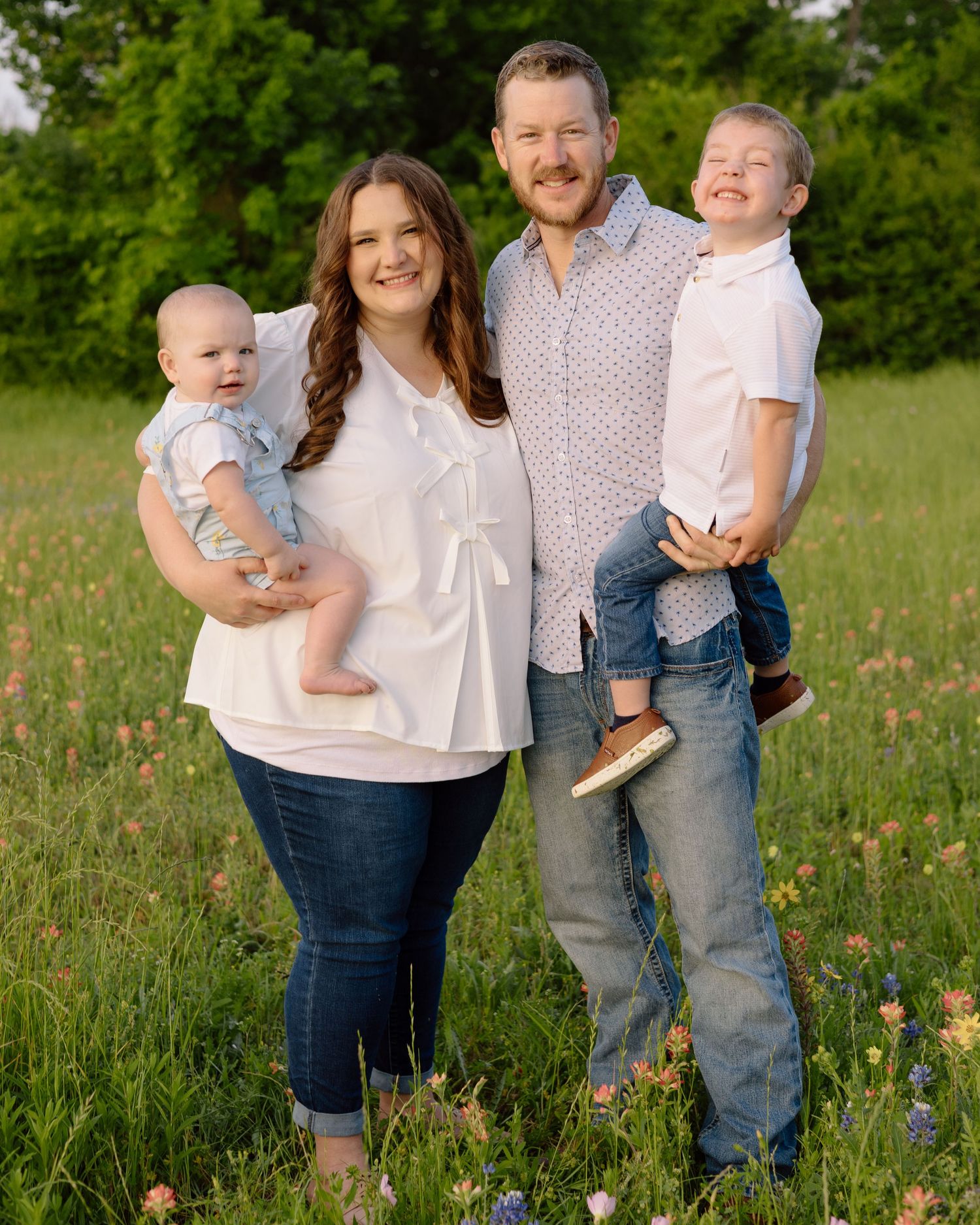 A joyful family poses together in a wildflower meadow on a sunny day wearing casual clothing.