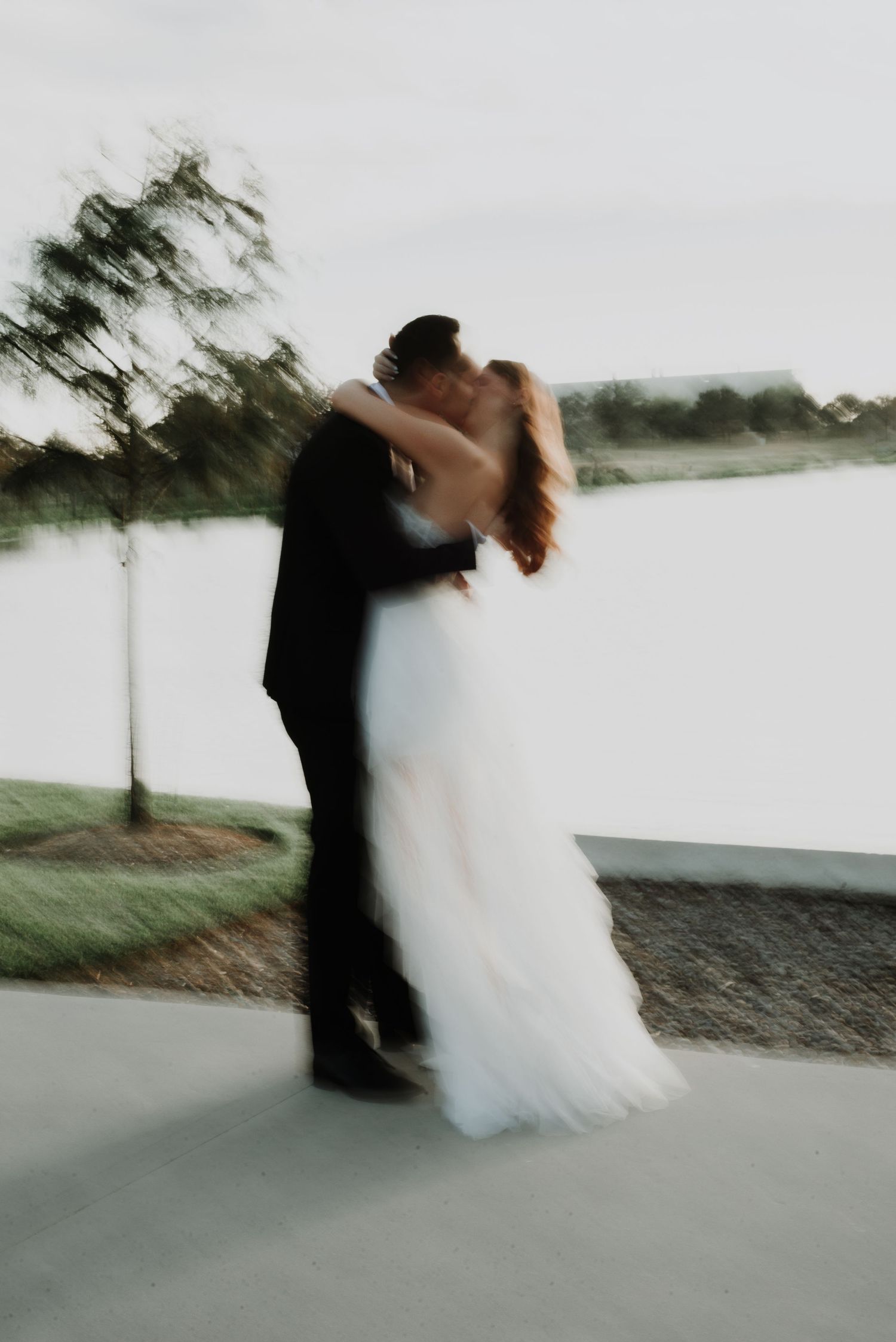 An artistic motion blur photo of a couple in formal attire embracing by the water.