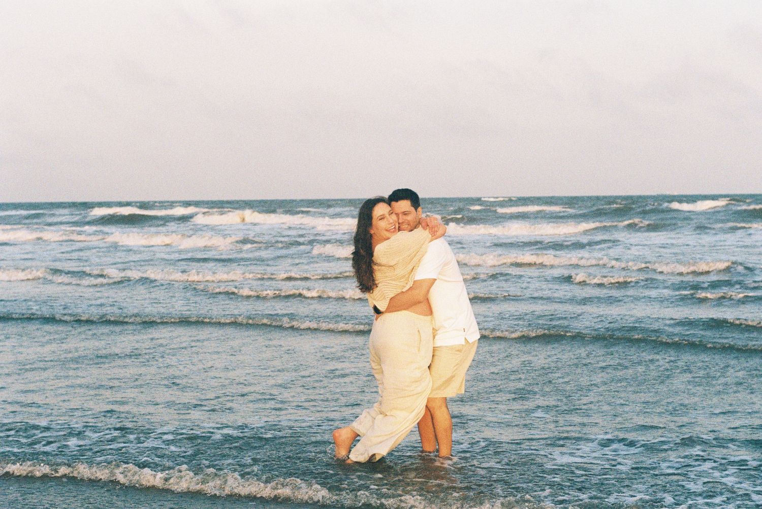 A couple embraces in the ocean waves during a romantic beach photoshoot.