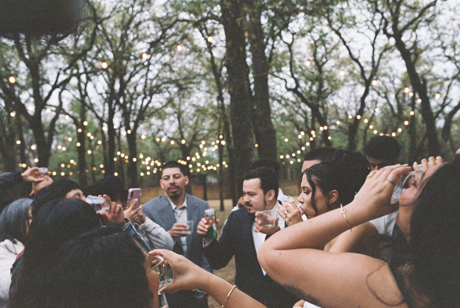 Wedding guests celebrating on a dance floor under string lights at an outdoor reception.