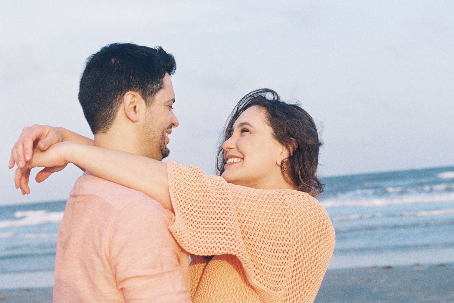 A couple embracing and laughing together on a beach at sunset.