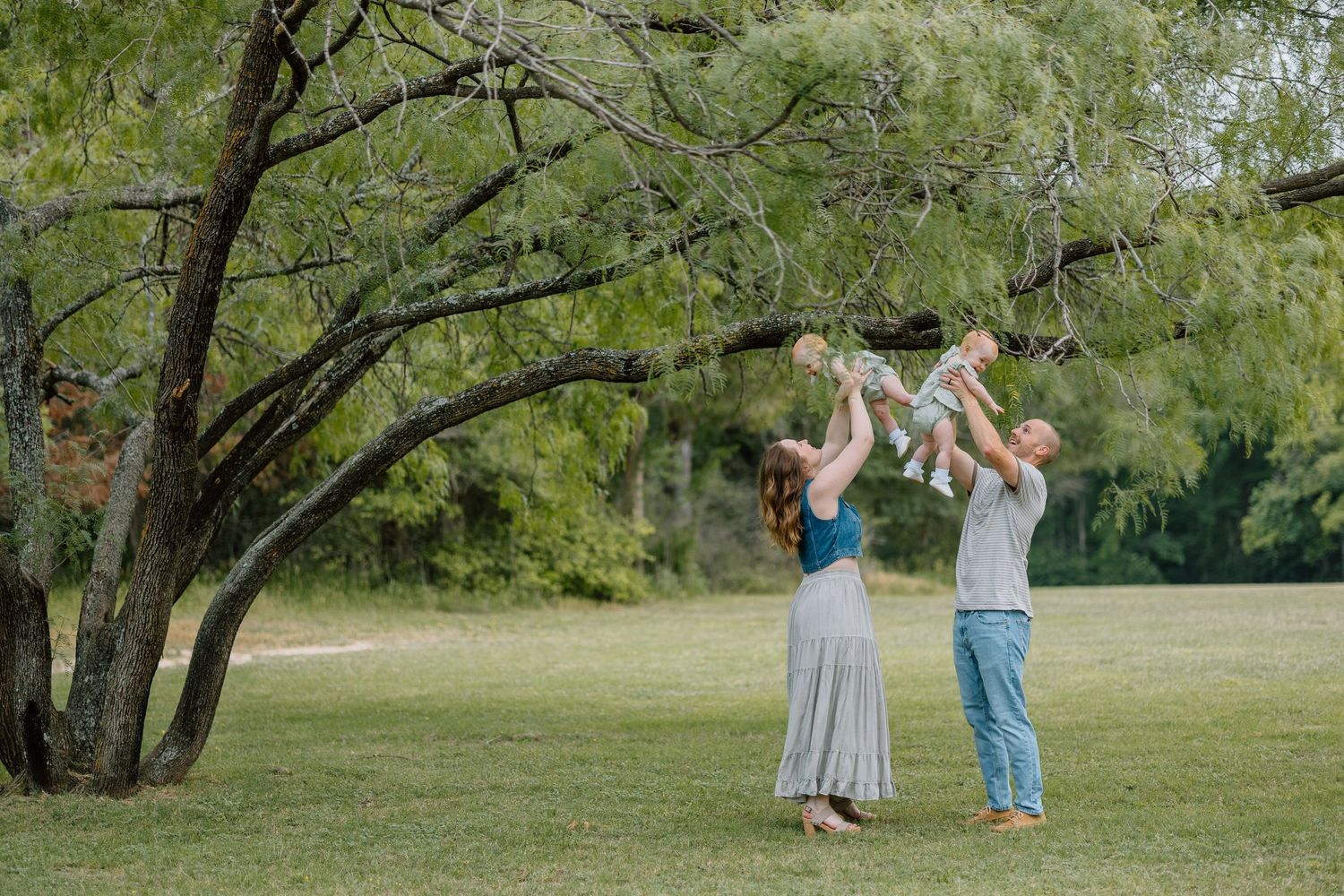 Two people stand on grass under a large tree in a park enjoying a warm sunny day outdoors together.