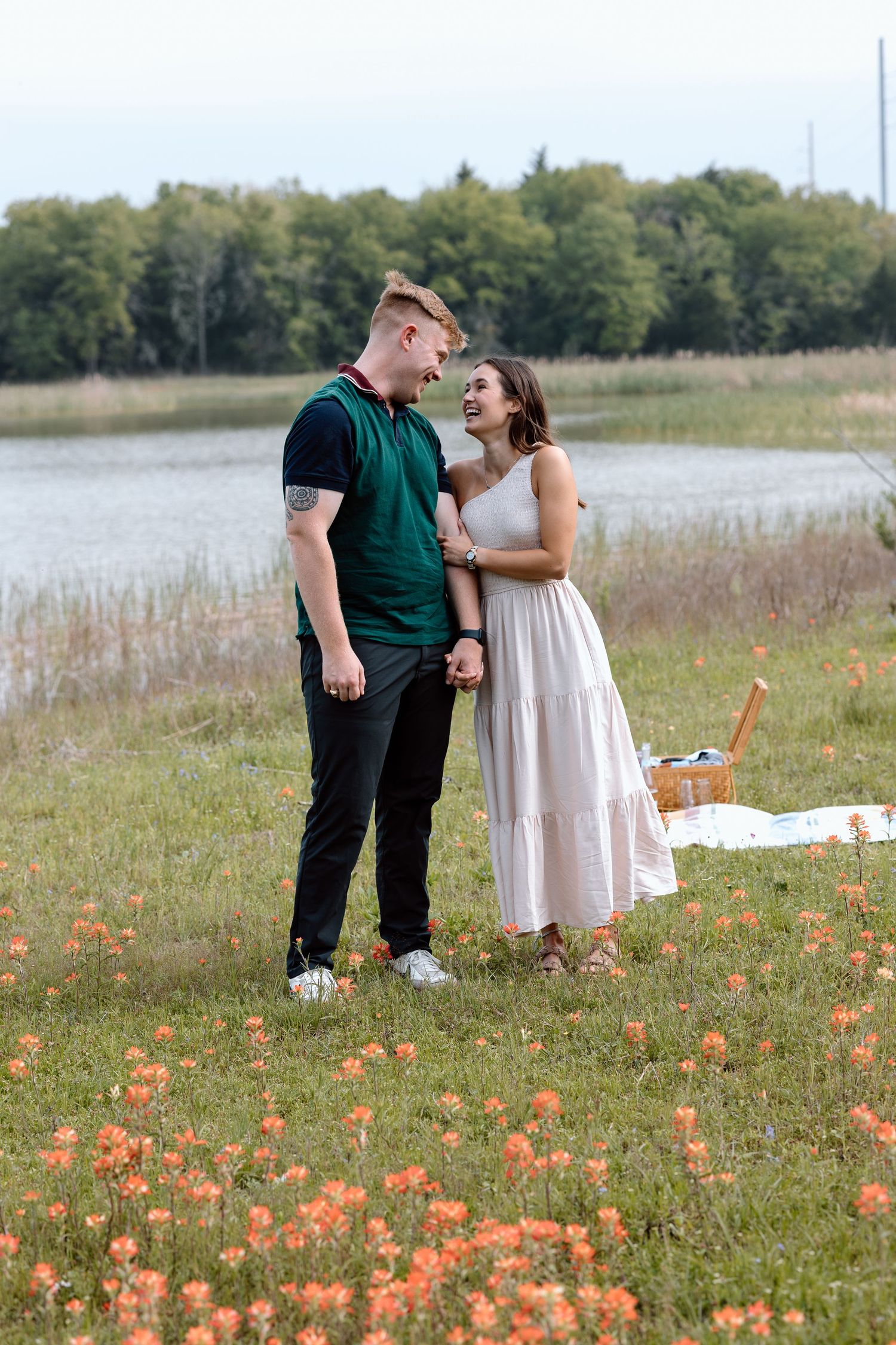 A couple shares a joyful moment in a meadow filled with orange flowers near a lake.