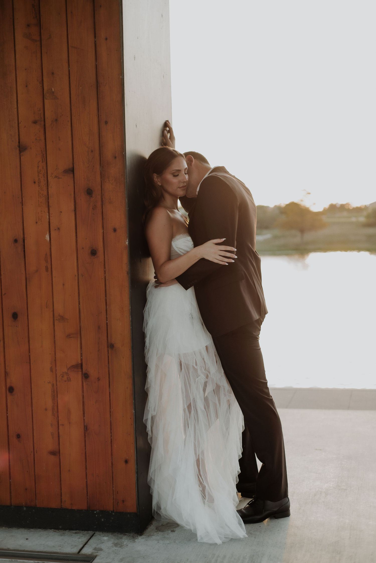 A romantic moment captured between a couple in formal attire against a wooden wall at sunset.
