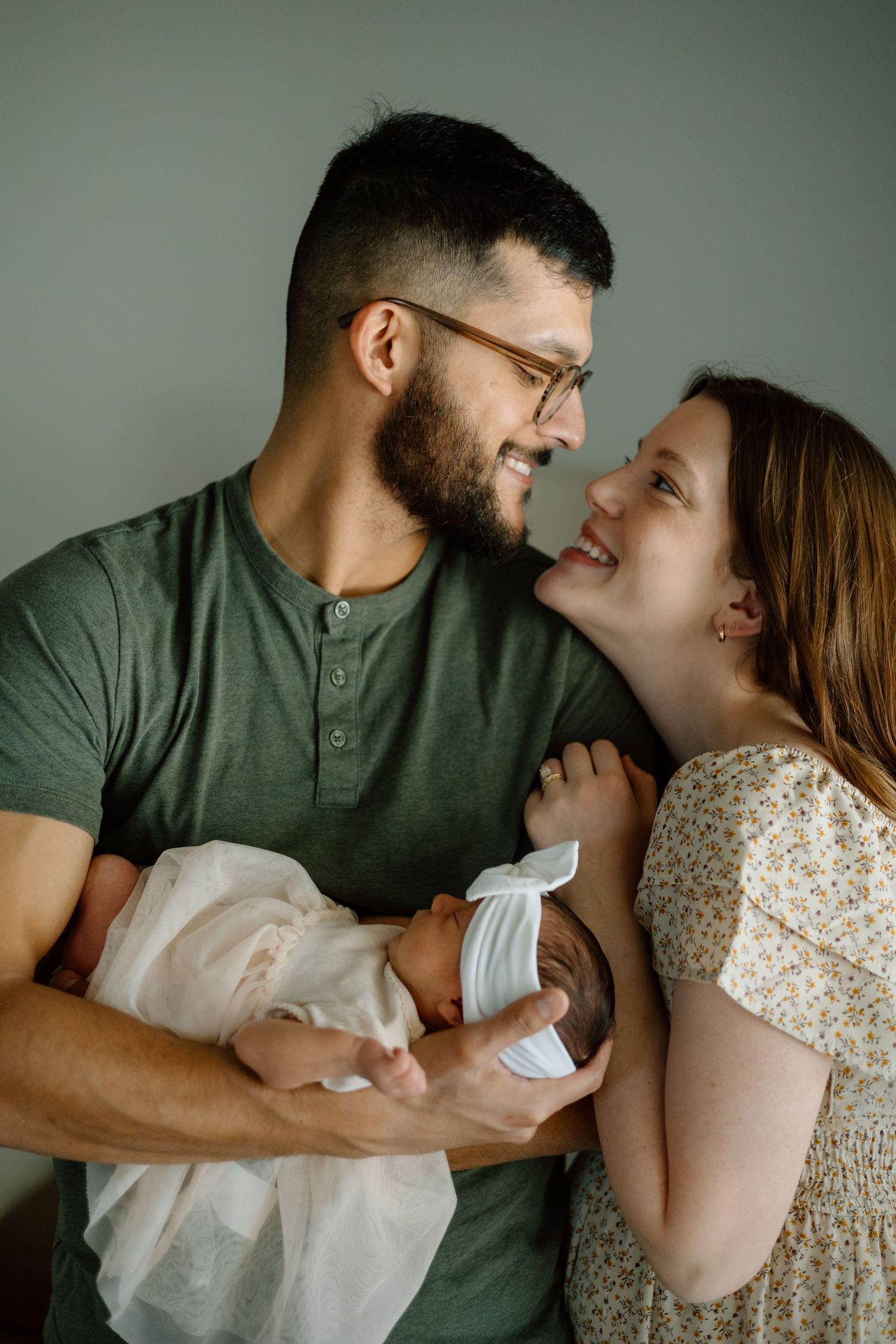 Intimate family moment as parents share joy while holding their swaddled newborn.
