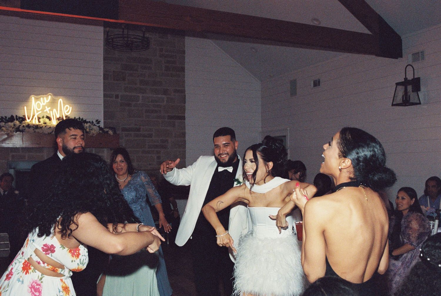 Wedding guests dancing and celebrating together at an indoor reception venue with brick walls and mood lighting.