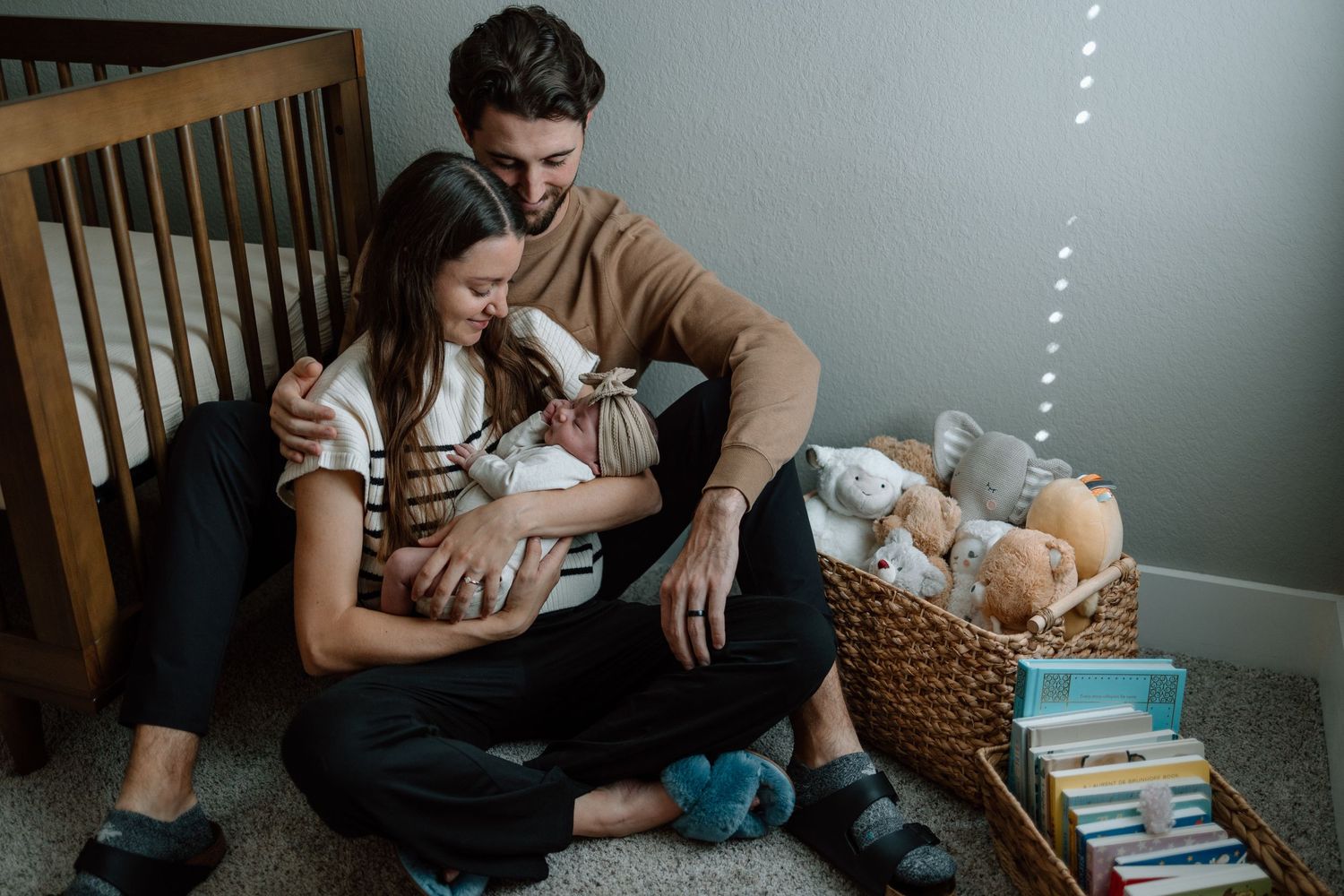 Family sitting together on carpet beside basket of toys and books with newborn baby.