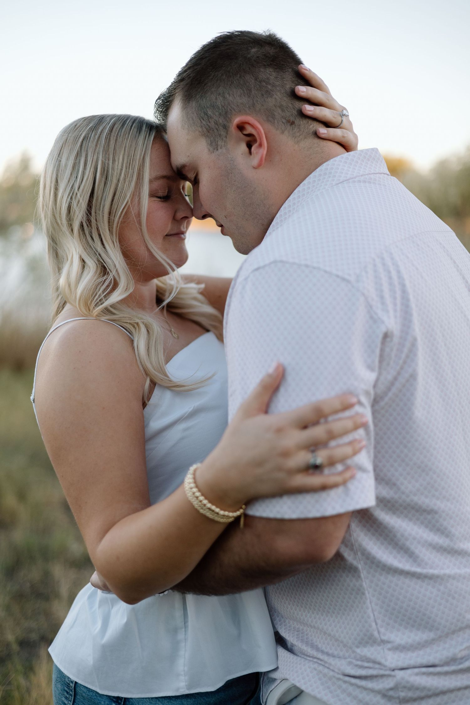 Couple sharing a romantic forehead touch embrace outdoors, woman in white top with blonde hair, man in white shirt.