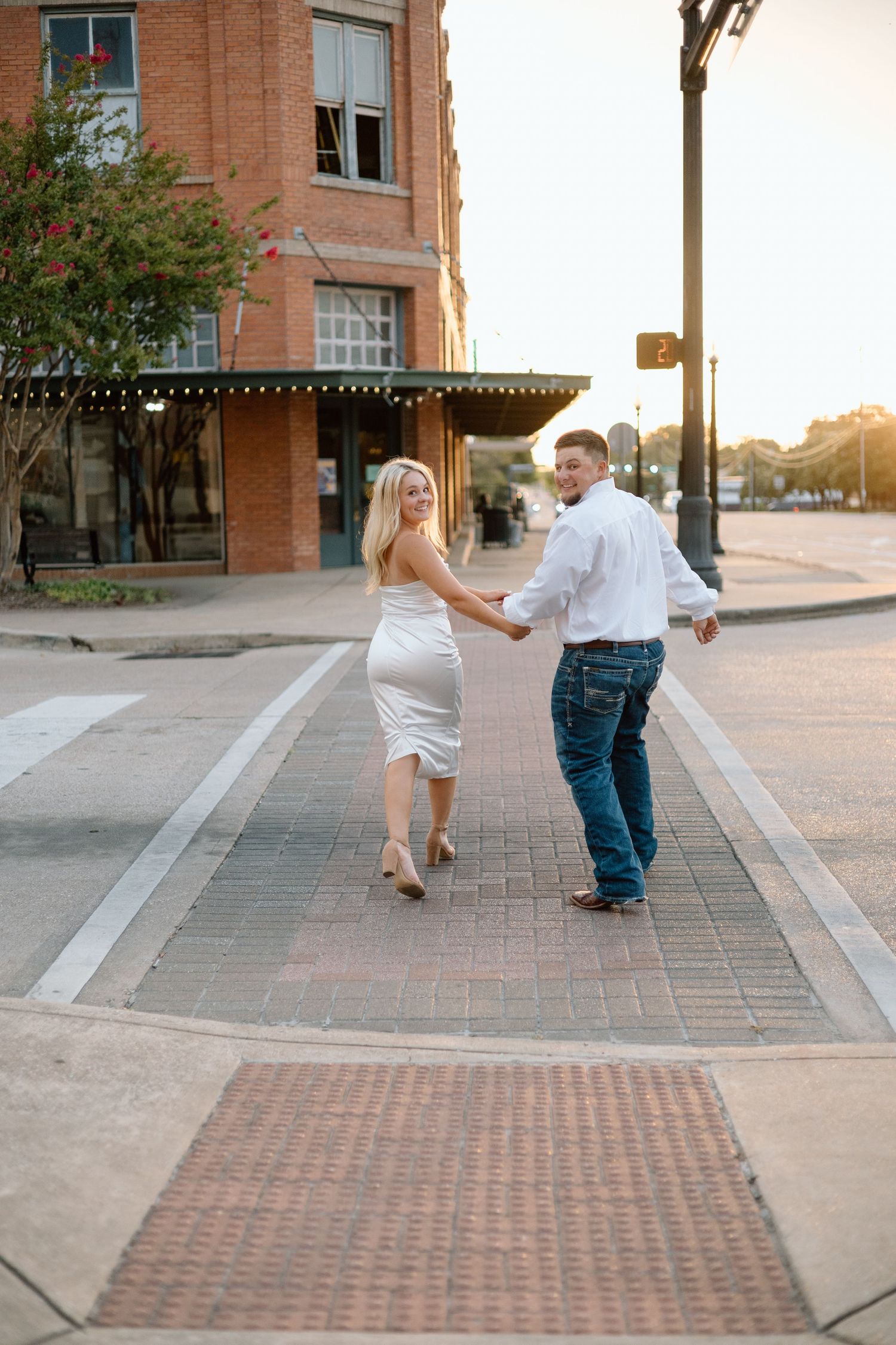 Couple holding hands walking across a brick crosswalk at sunset in a charming downtown street.