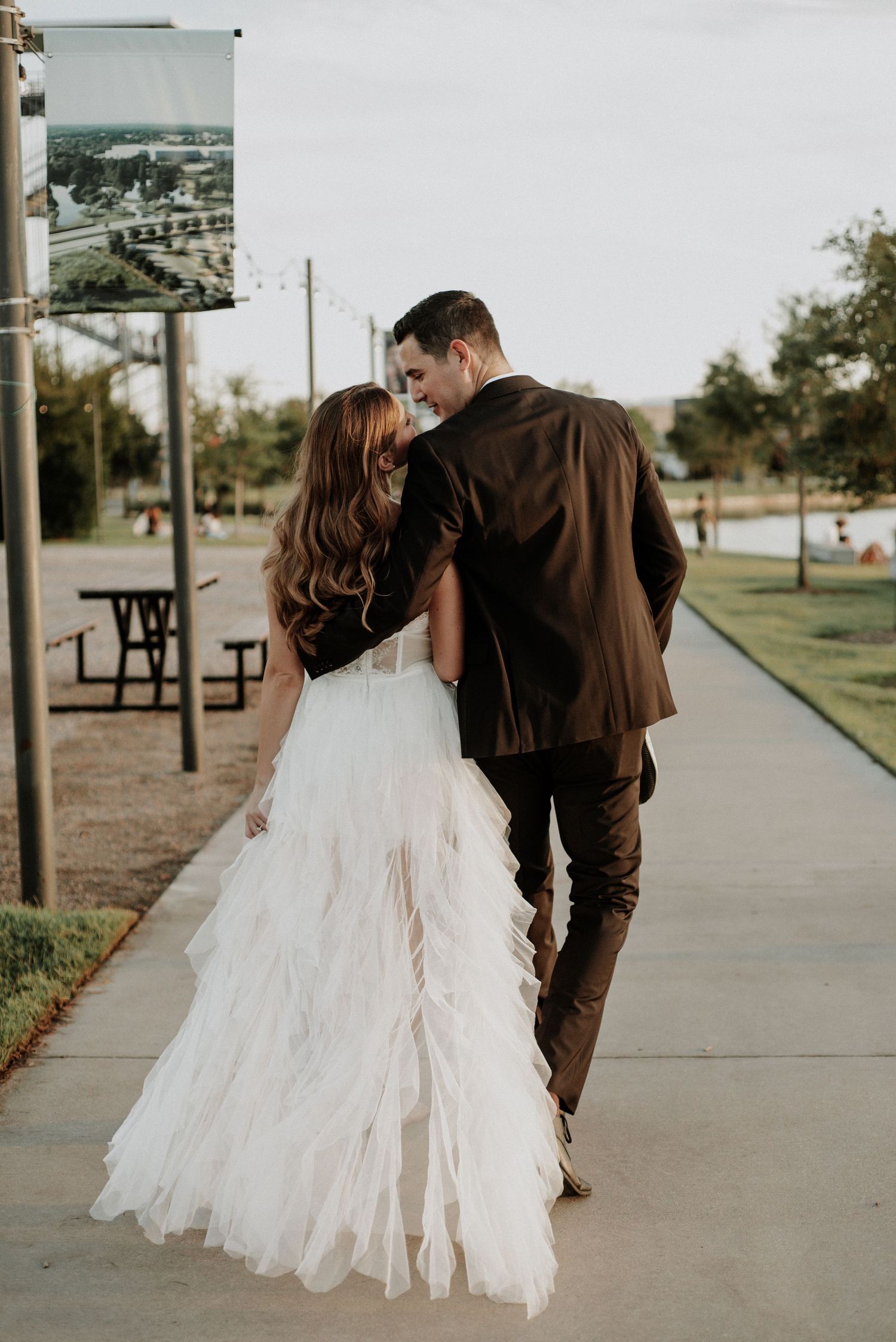 A couple walks together on a pathway, with the bride's flowing white dress trailing behind.