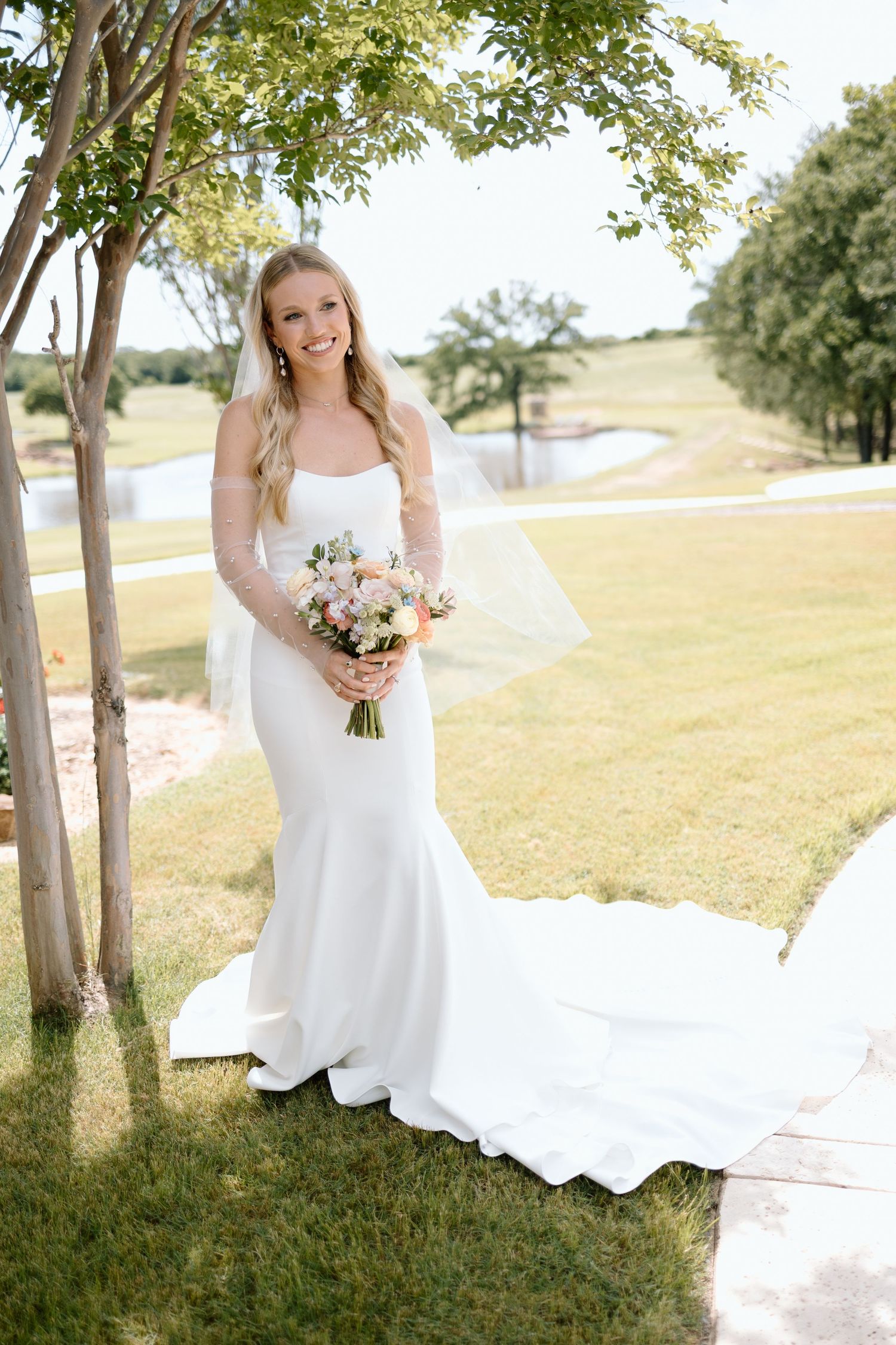 Elegant white wedding dress with long train photographed outdoors in a scenic garden setting.