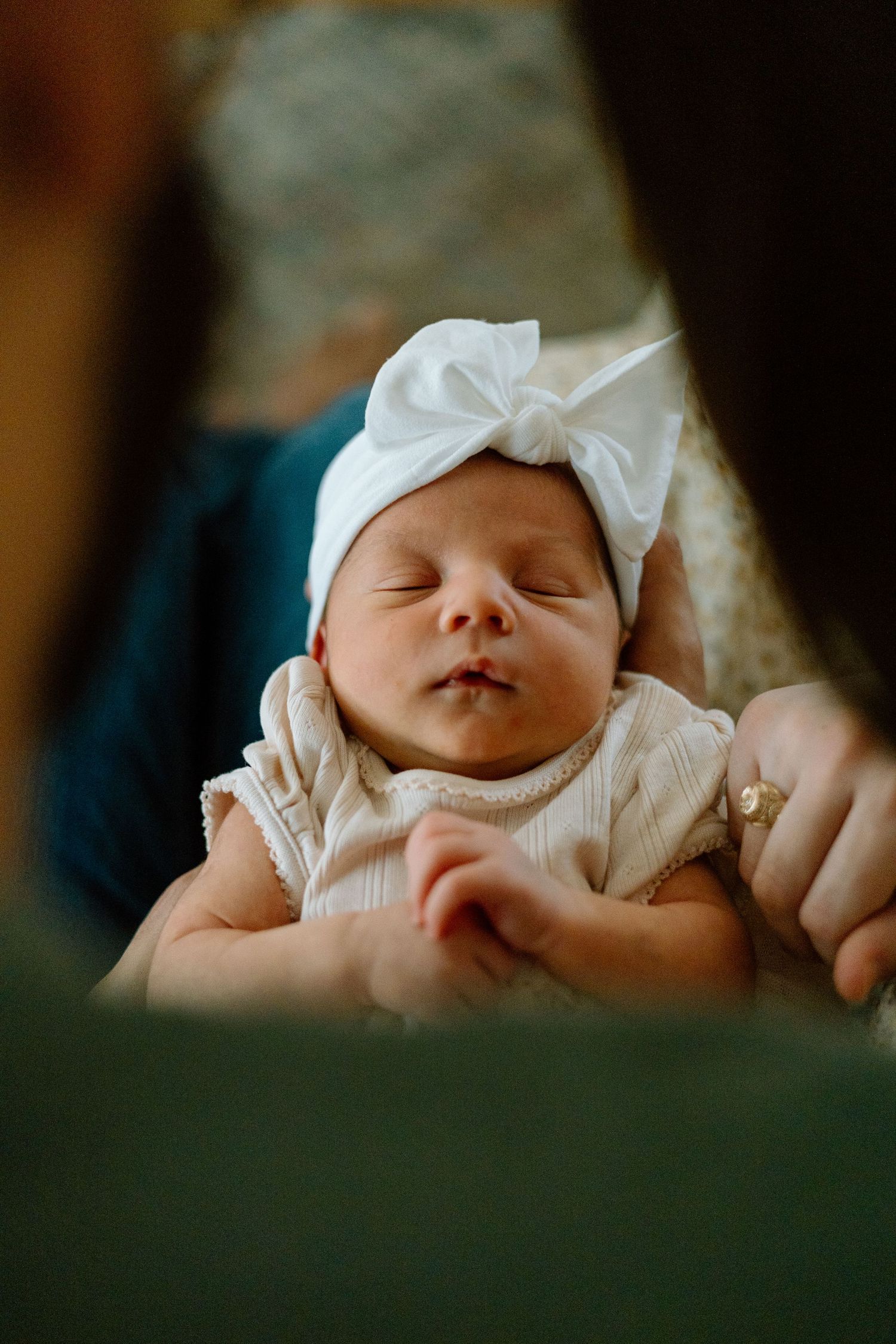 Close-up of peaceful sleeping newborn wearing white bow headband and ruffled outfit.