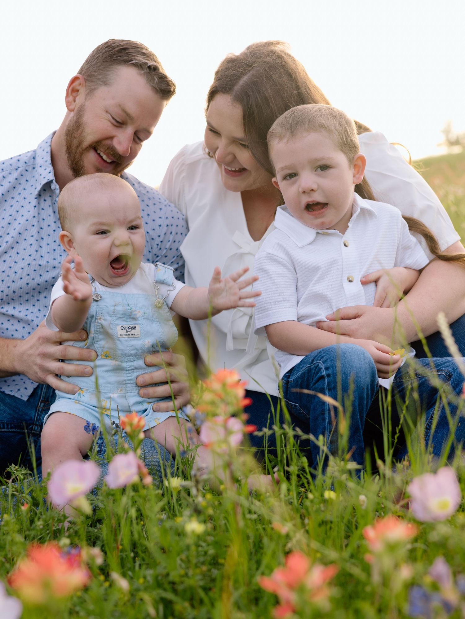 Family enjoying a joyful moment together while sitting in a wildflower meadow during golden hour.