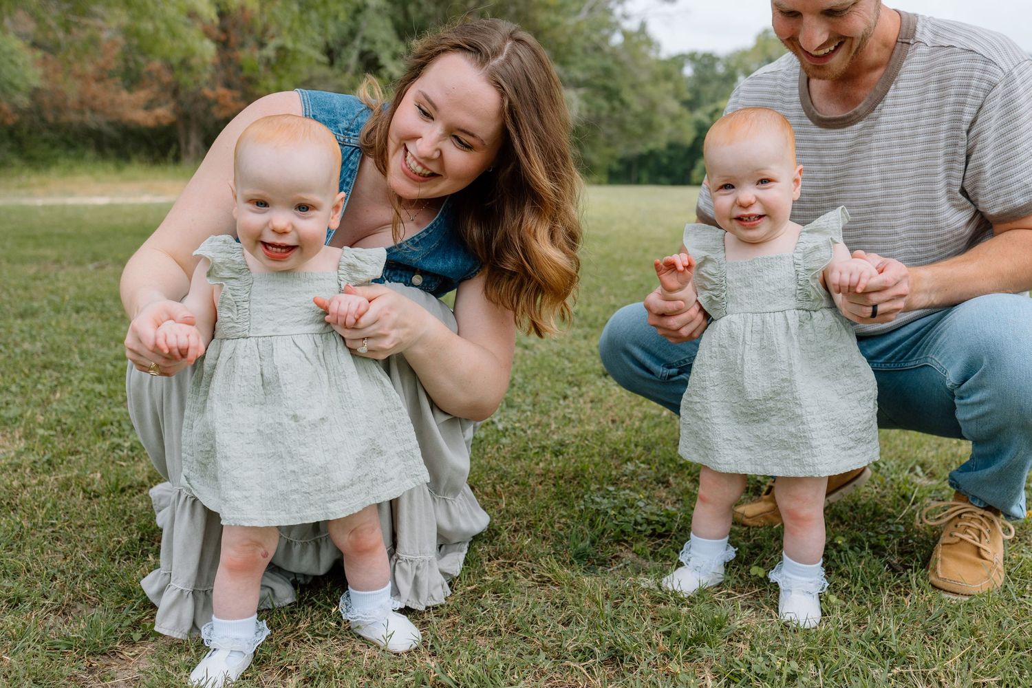 Happy family enjoying outdoor time with twin babies in matching blue dresses on a grassy lawn.