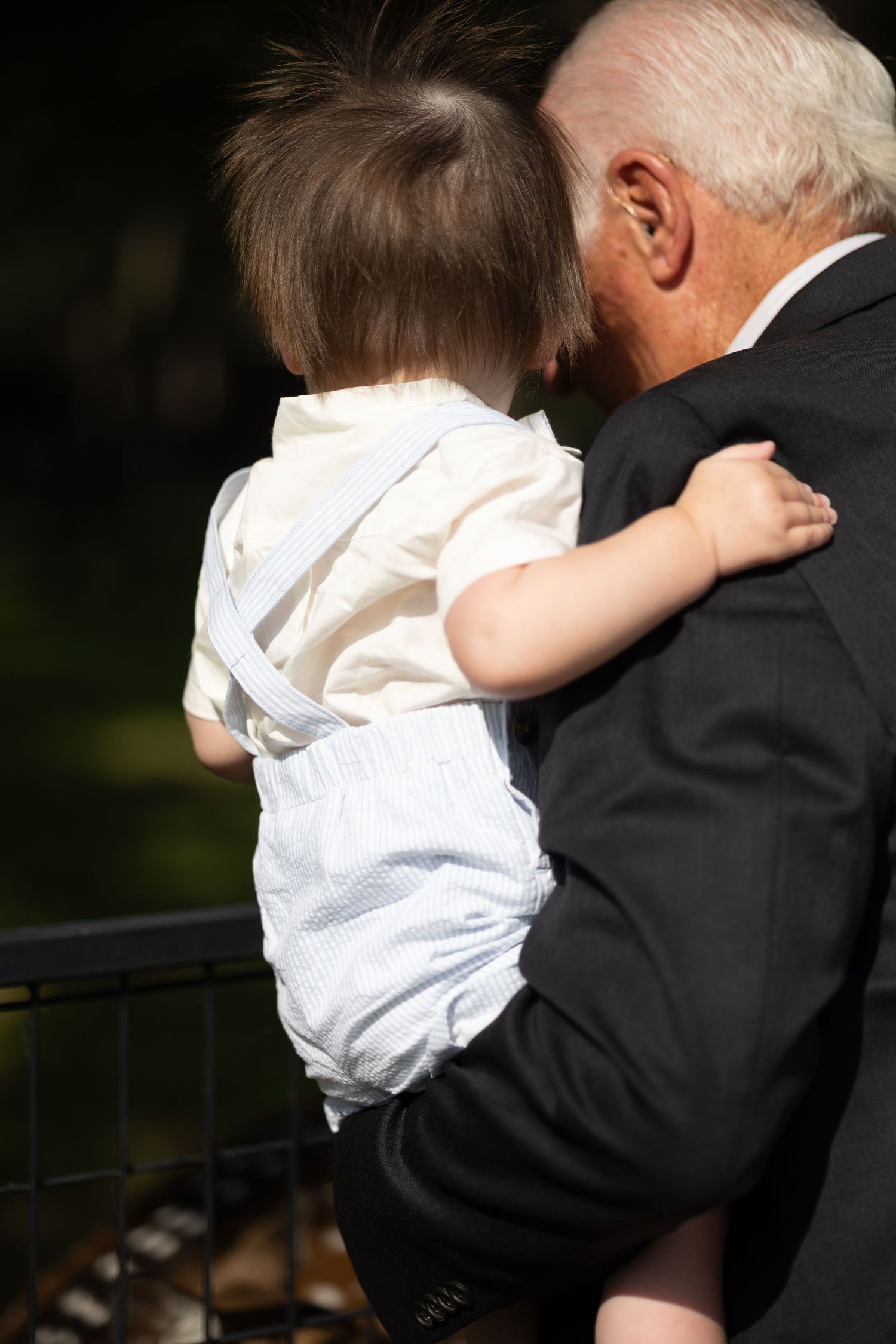 A touching moment between a young child in white and elderly person in formal attire.