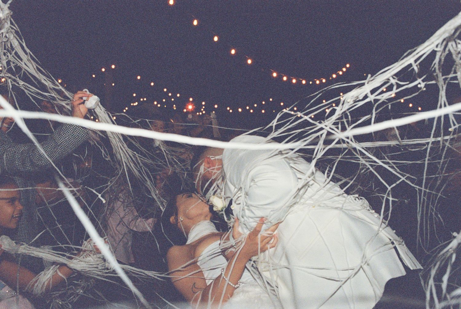 Wedding guests celebrating under decorative streamers and string lights at night.