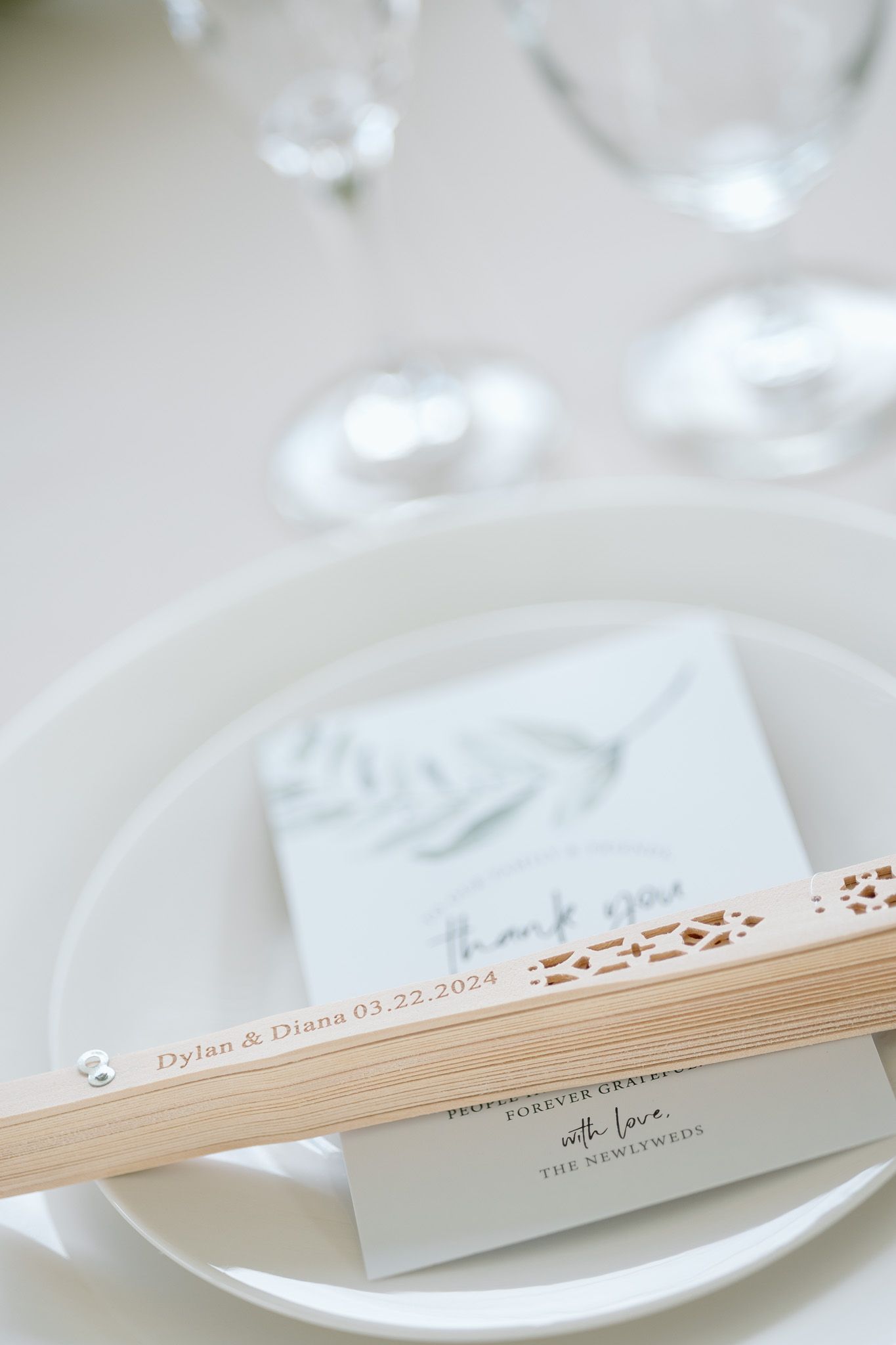 Elegant white paper menu and wooden fan placed on a formal table setting with crystal glassware.