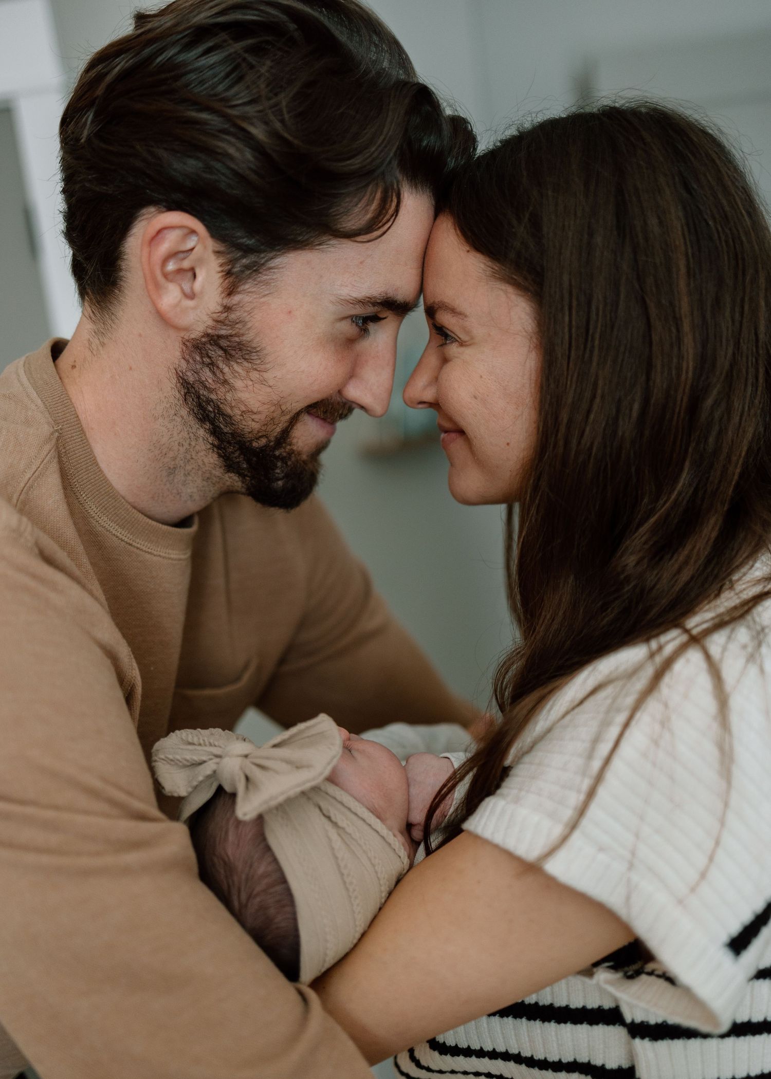 Intimate family moment with new parents sharing a close embrace while holding their swaddled baby.