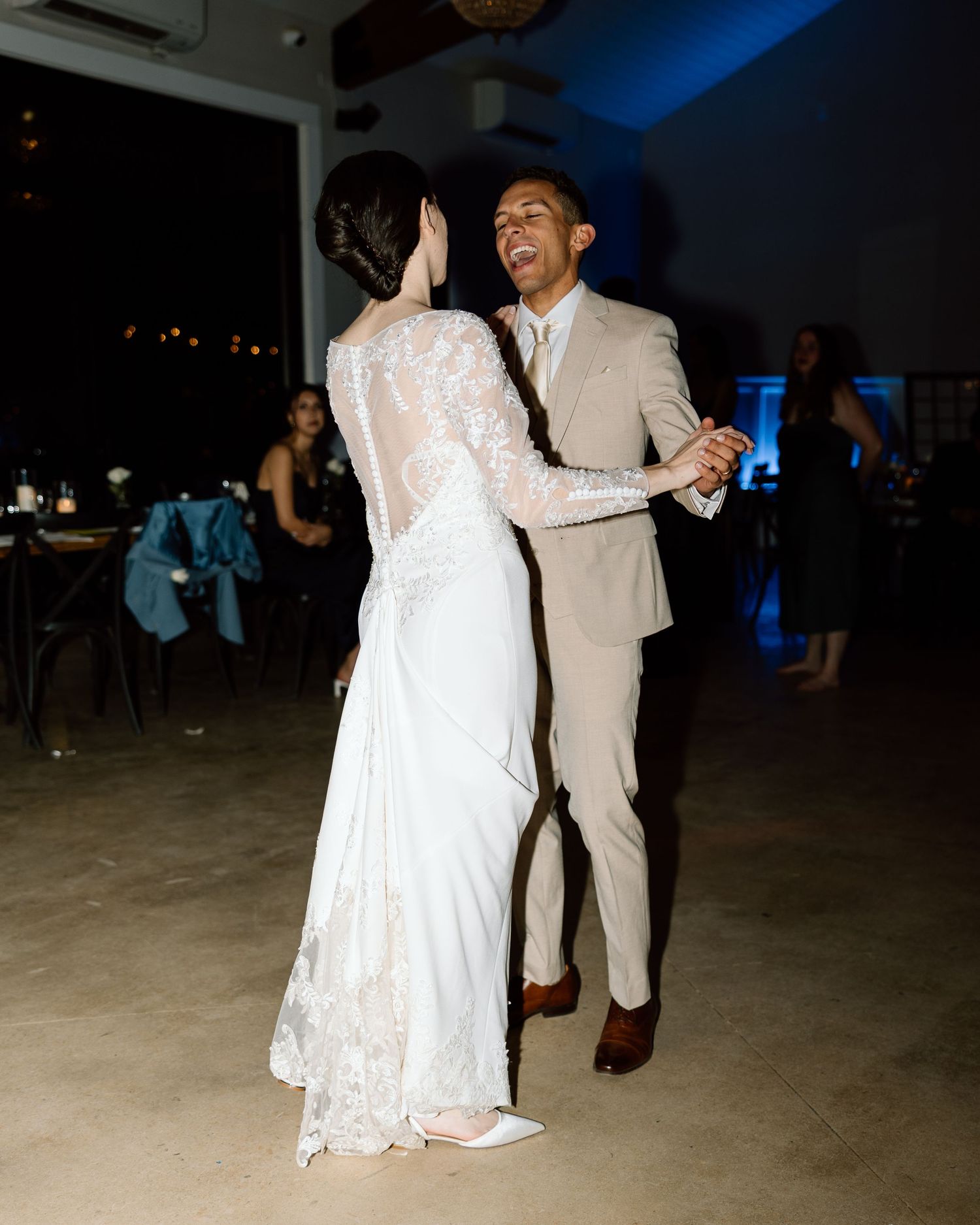 Couple sharing a joyful first dance at evening wedding reception under blue lights.