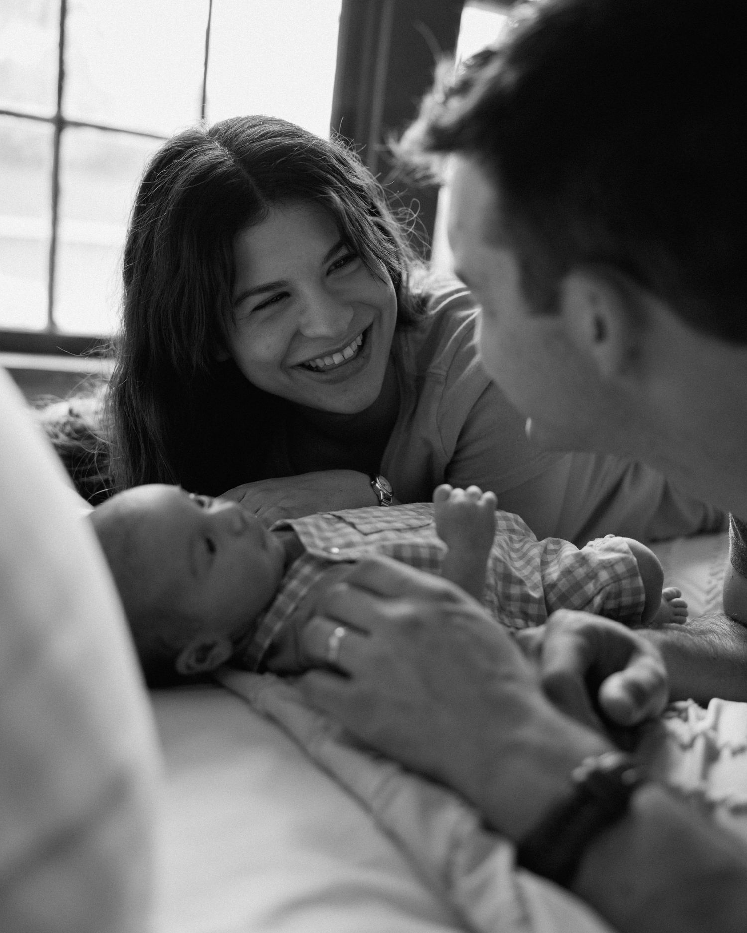 Smiling mother and father gazing lovingly at their newborn baby in black and white photo.