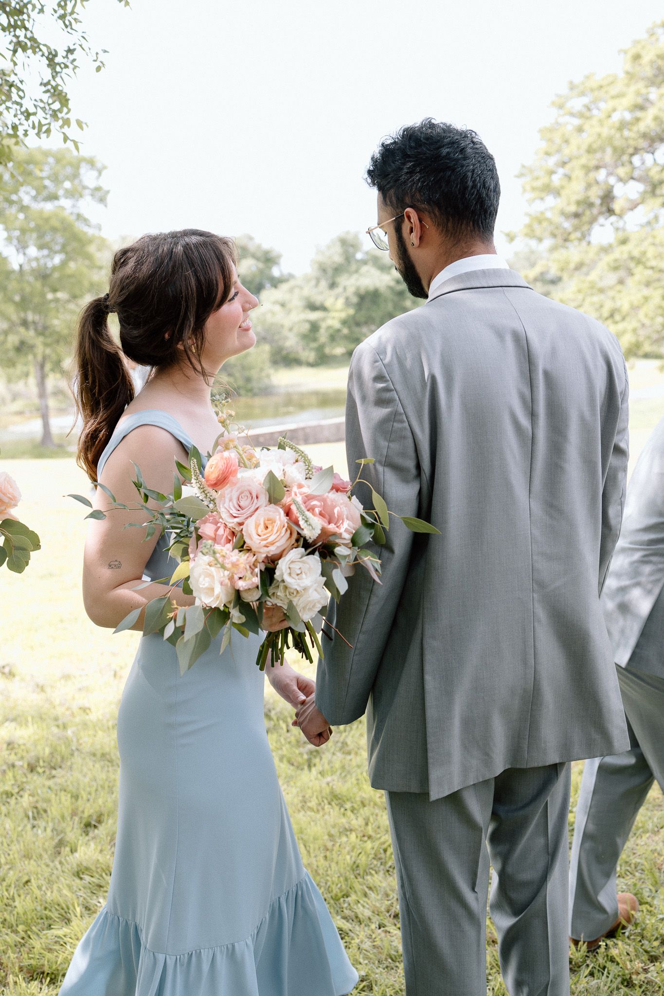 A couple in formal attire sharing a moment outdoors with peach and white bouquet.