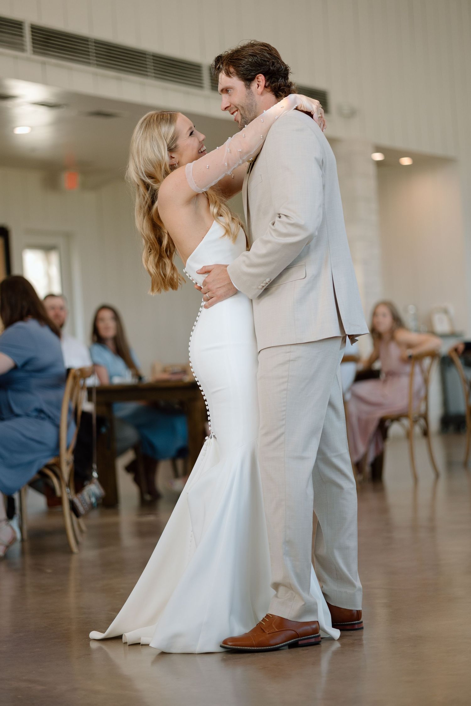 A wedding couple shares their first dance in a reception hall with guests watching.