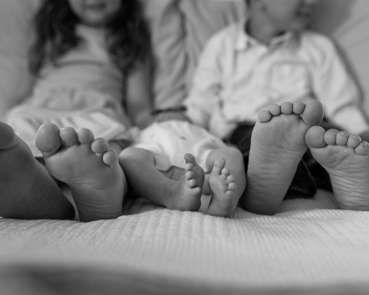 Black and white photo of three children lying down showing their bare feet on a soft bed surface.