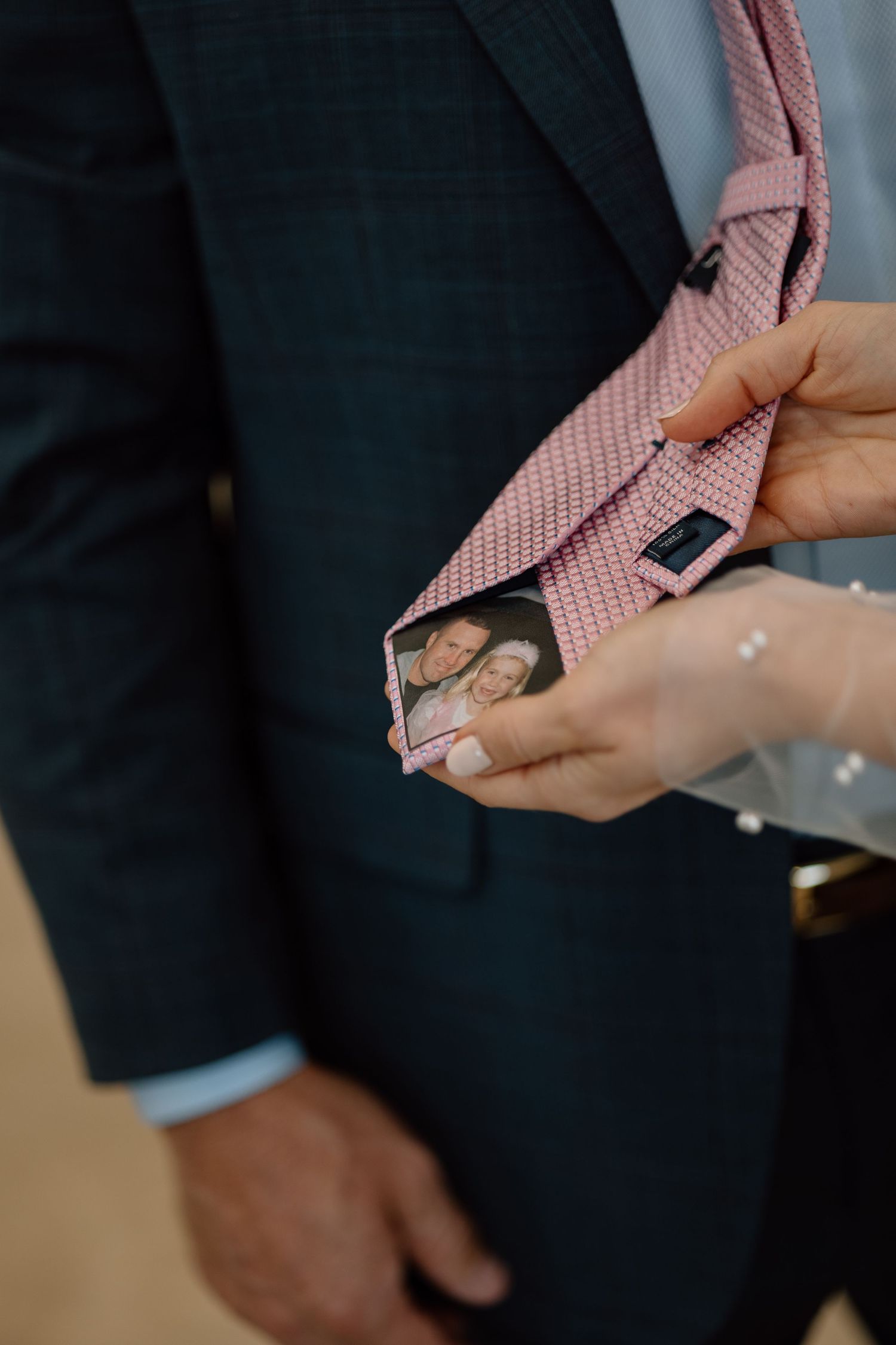 Close-up of hands pinning a photo inside pink tie during wedding preparation.