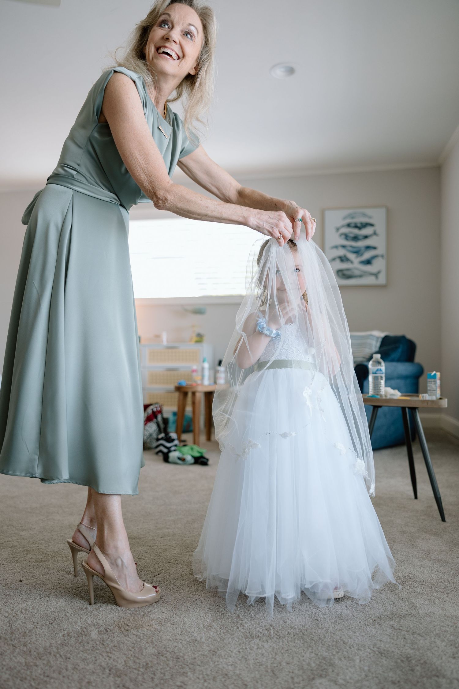 A woman in a sage green dress helps with a white tulle flower girl dress.