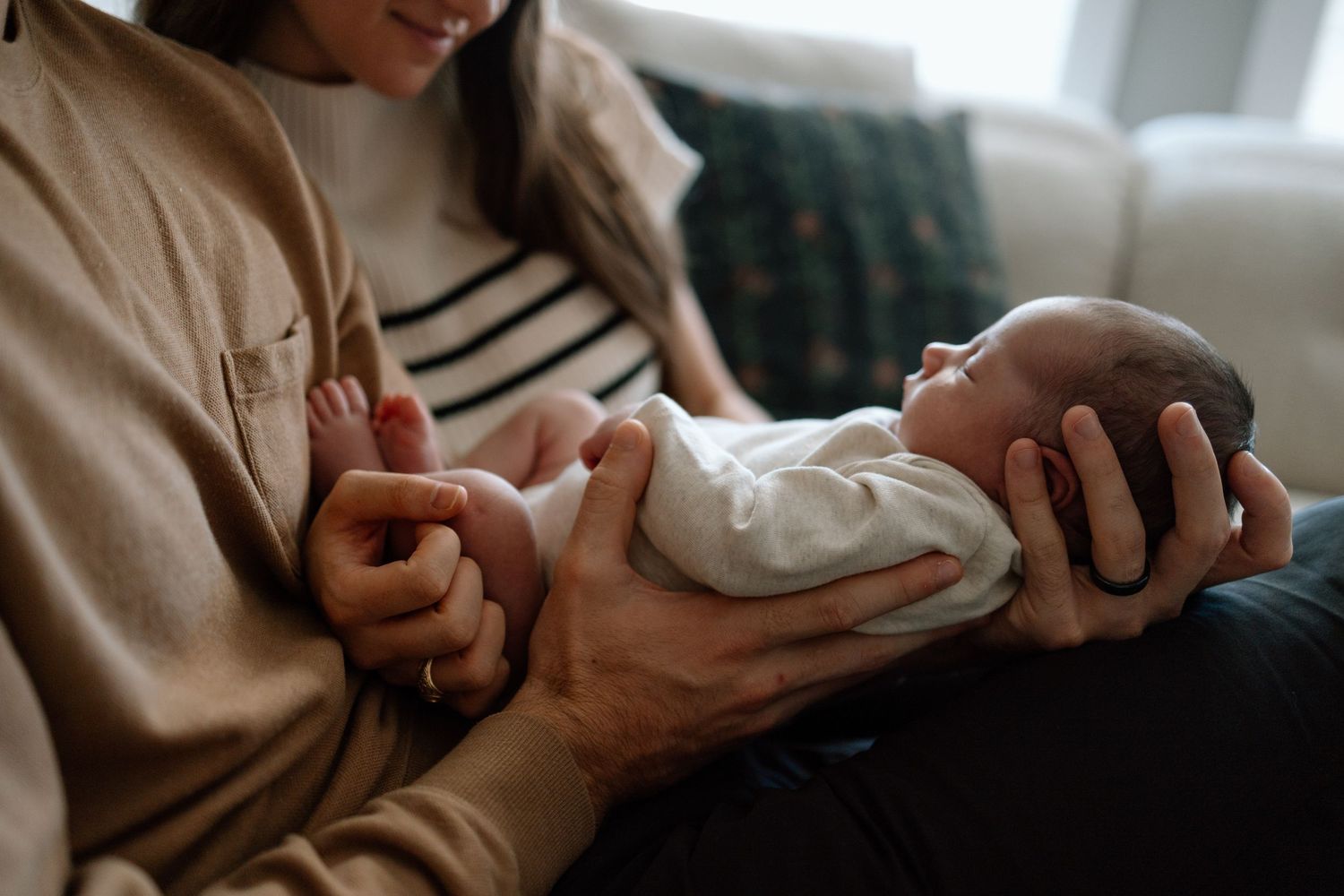 Close-up shot of newborn baby being cradled in caregiver's arms on couch.