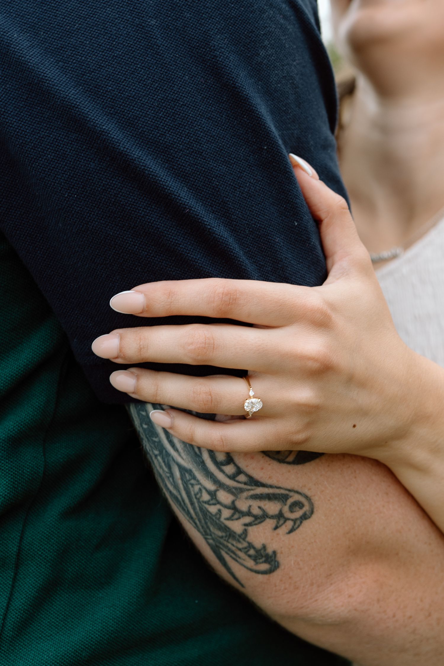 Close-up of hands showing an engagement ring and tattoo as a couple embraces.