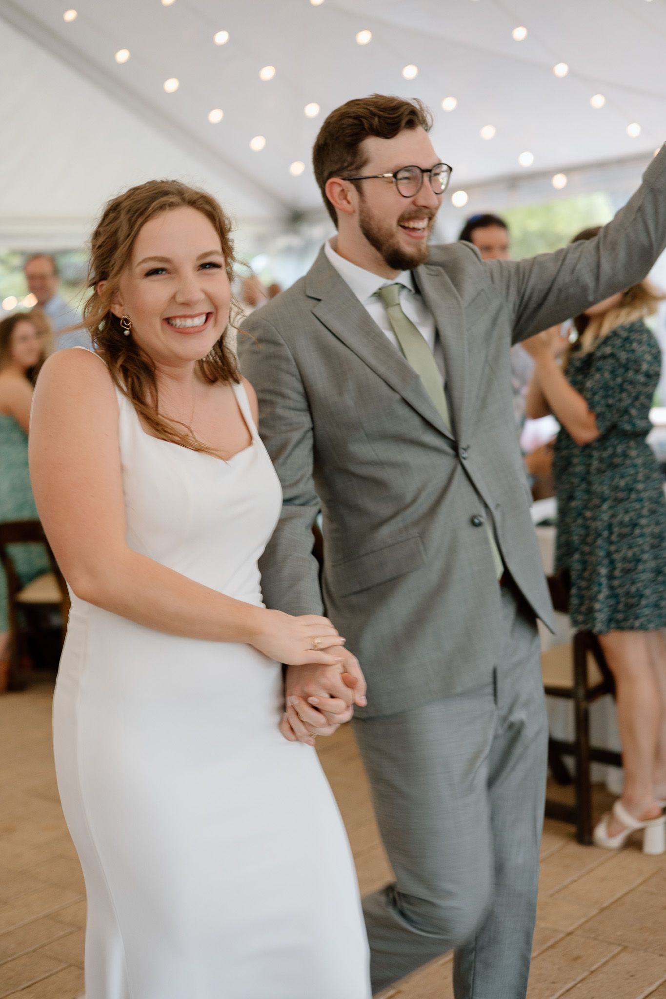 Joyful couple celebrating during their wedding reception under a tent with twinkle lights.