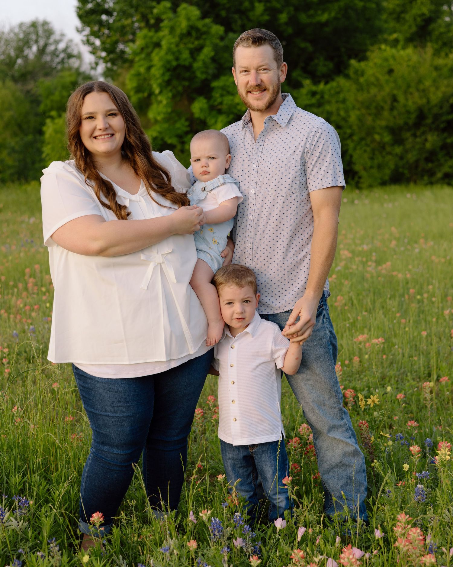 Family stands together in a flowering meadow wearing coordinated casual outfits on a sunny spring day.