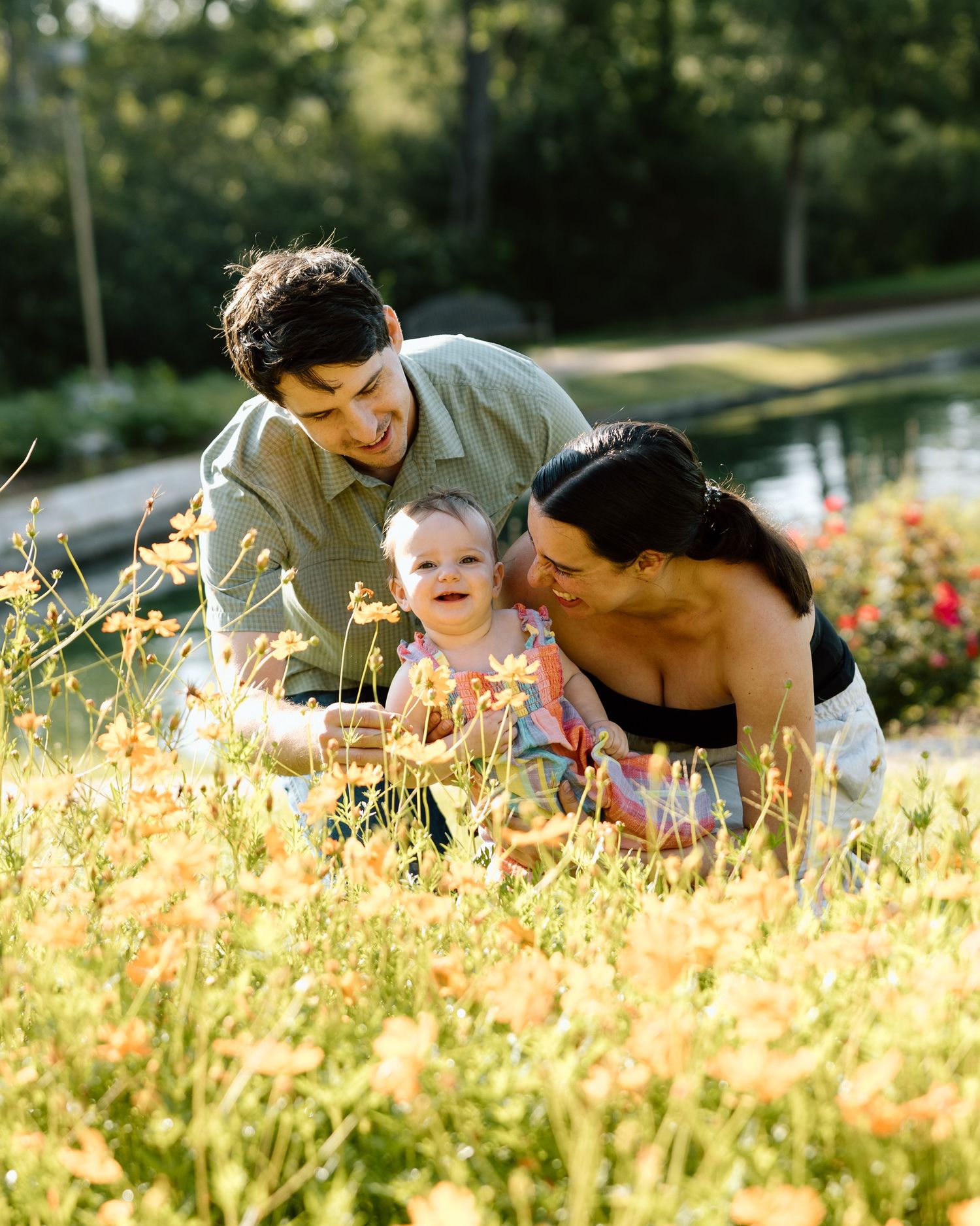 Family with baby enjoying yellow wildflowers in a sunny garden park, smiling and bonding together outdoors.